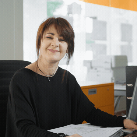 Une femme en chemise noire sourit assise à un bureau