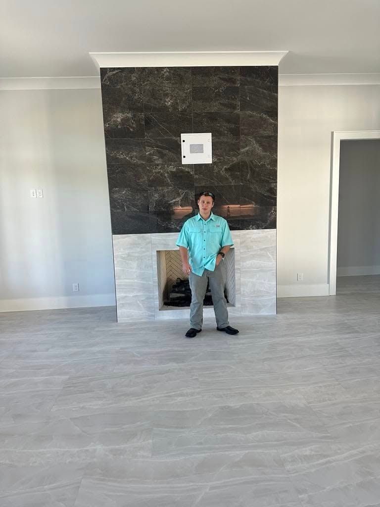 Man standing in front of fireplace in empty room. Fireplace has dark tile and gray stone.