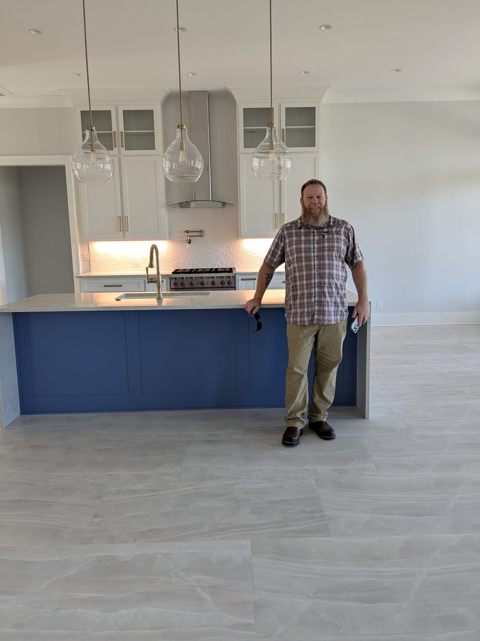 Man standing in a new kitchen; blue island, white cabinets, silver fixtures.