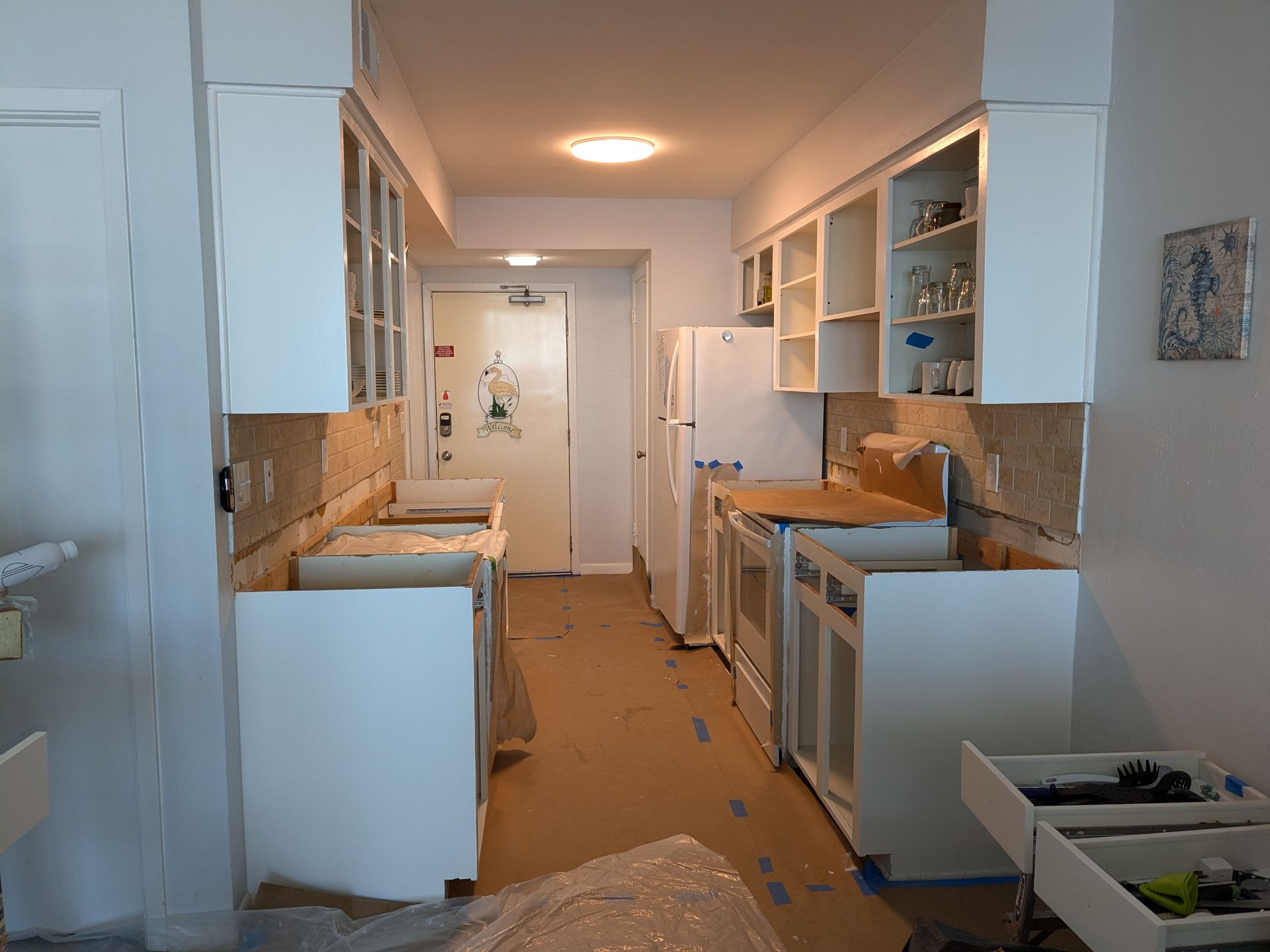 Kitchen remodel in progress: white cabinets, appliances, exposed walls, narrow hallway.