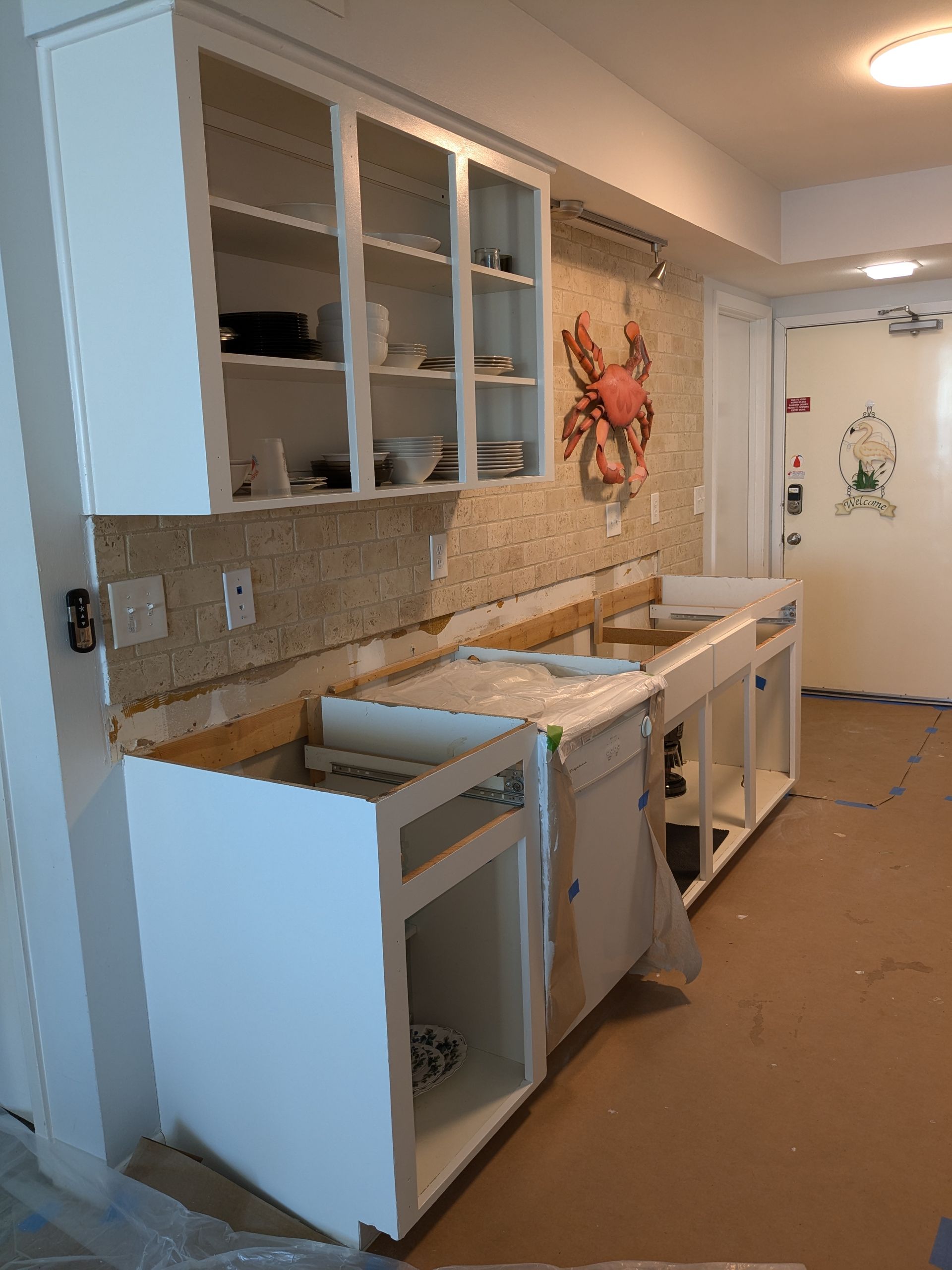 Kitchen cabinets under construction; white cabinets, exposed wall, crab art.