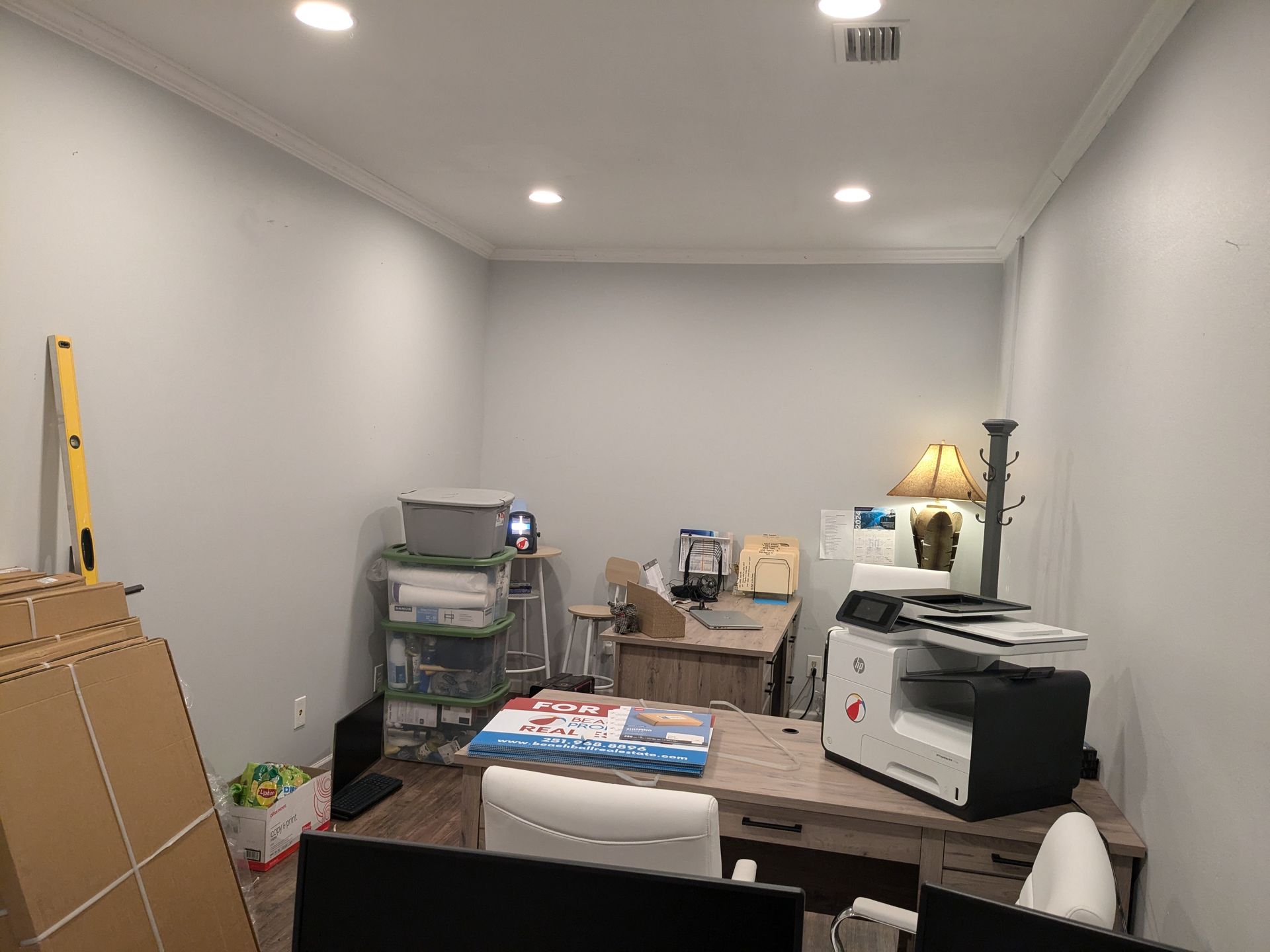 An empty office space with gray walls, desk, printer, boxes, and miscellaneous items.