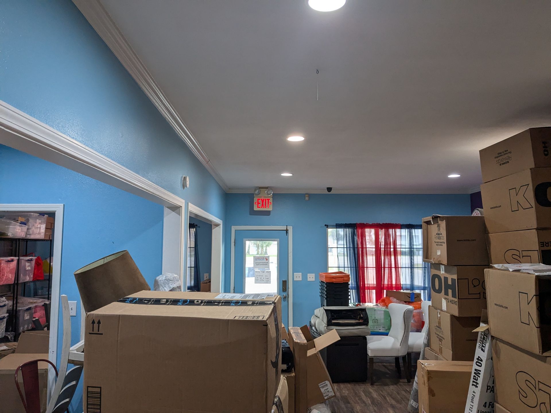 Interior view of a room with blue walls, boxes, and an exit sign visible.