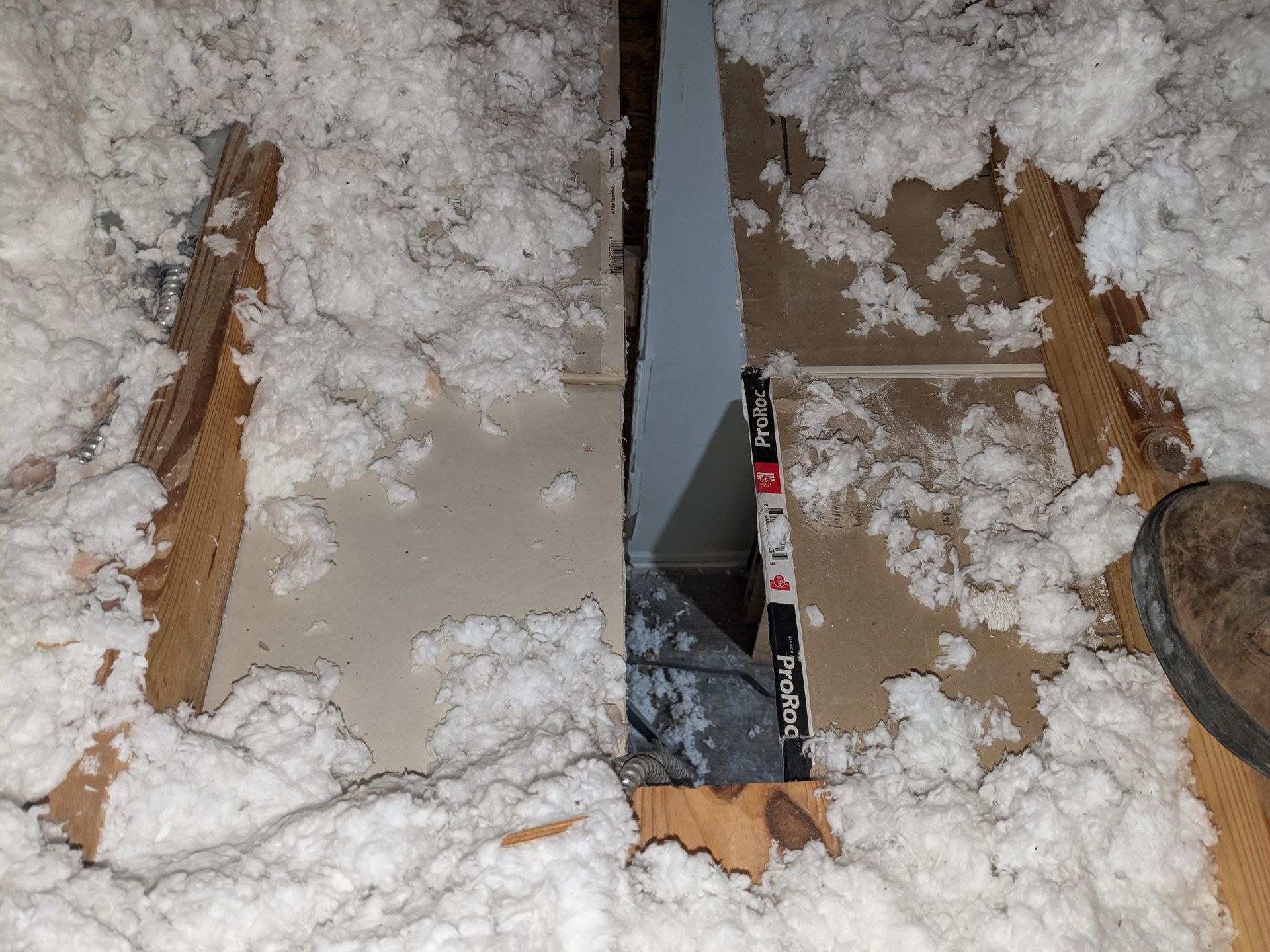 Hole in attic floor with insulation and a measuring stick visible.