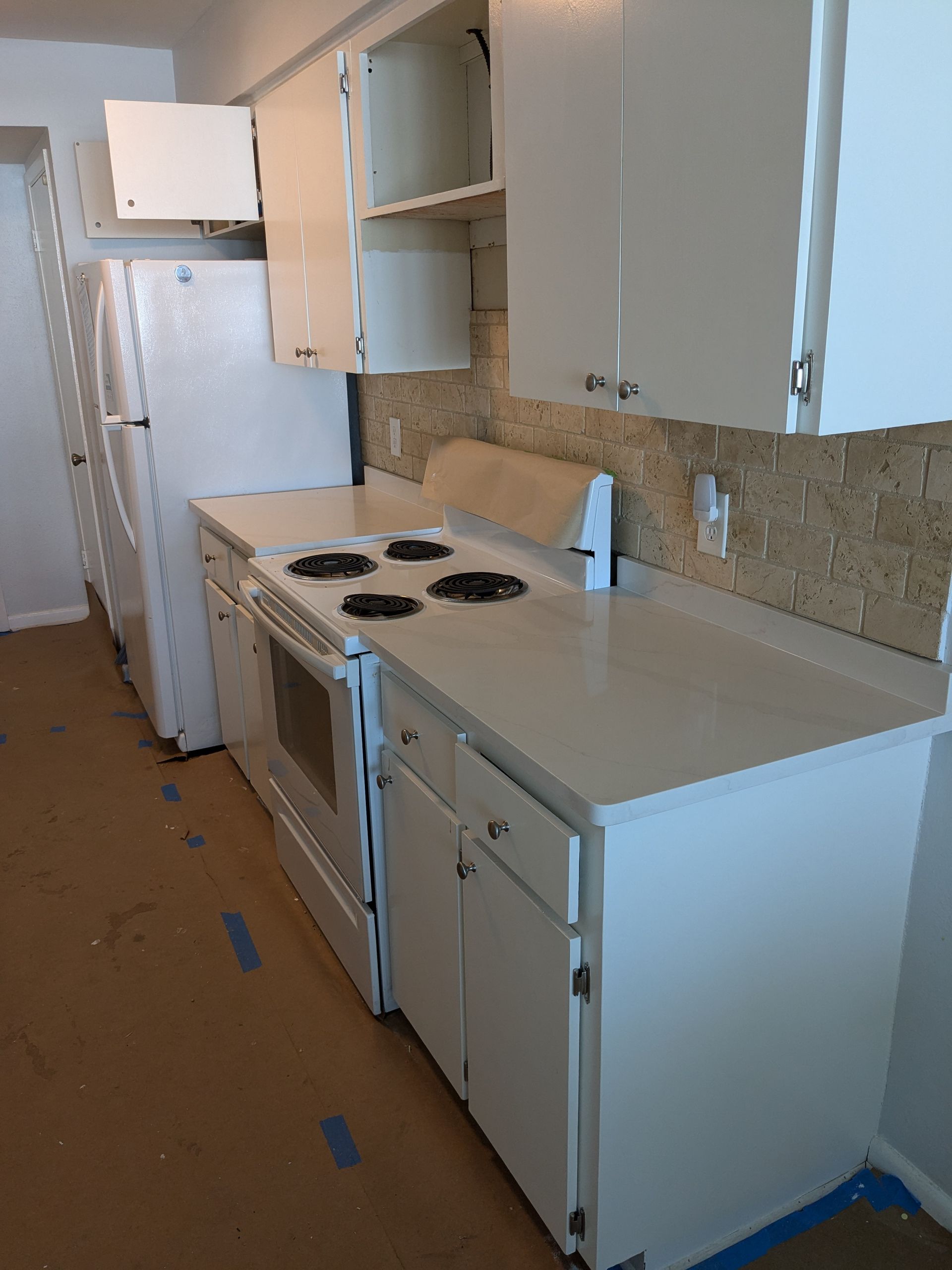 White kitchen with a stove, cabinets, refrigerator, and backsplash.