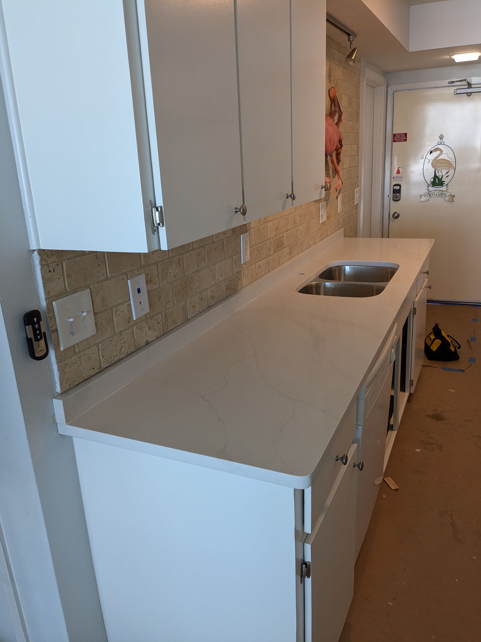 White kitchen cabinets with light countertops, sink, and backsplash. Doorway in the background.