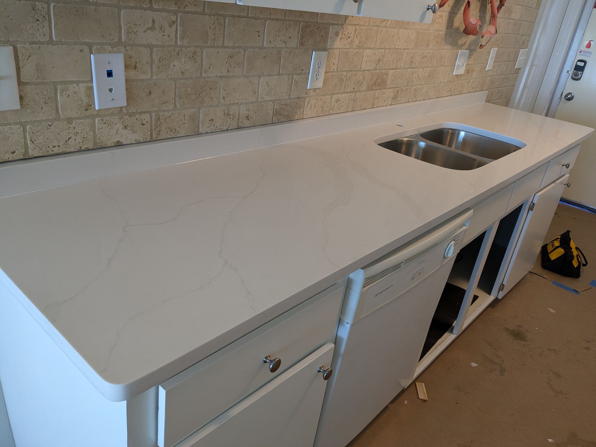 White countertop with a sink, set on white cabinets, against a tan brick backsplash.