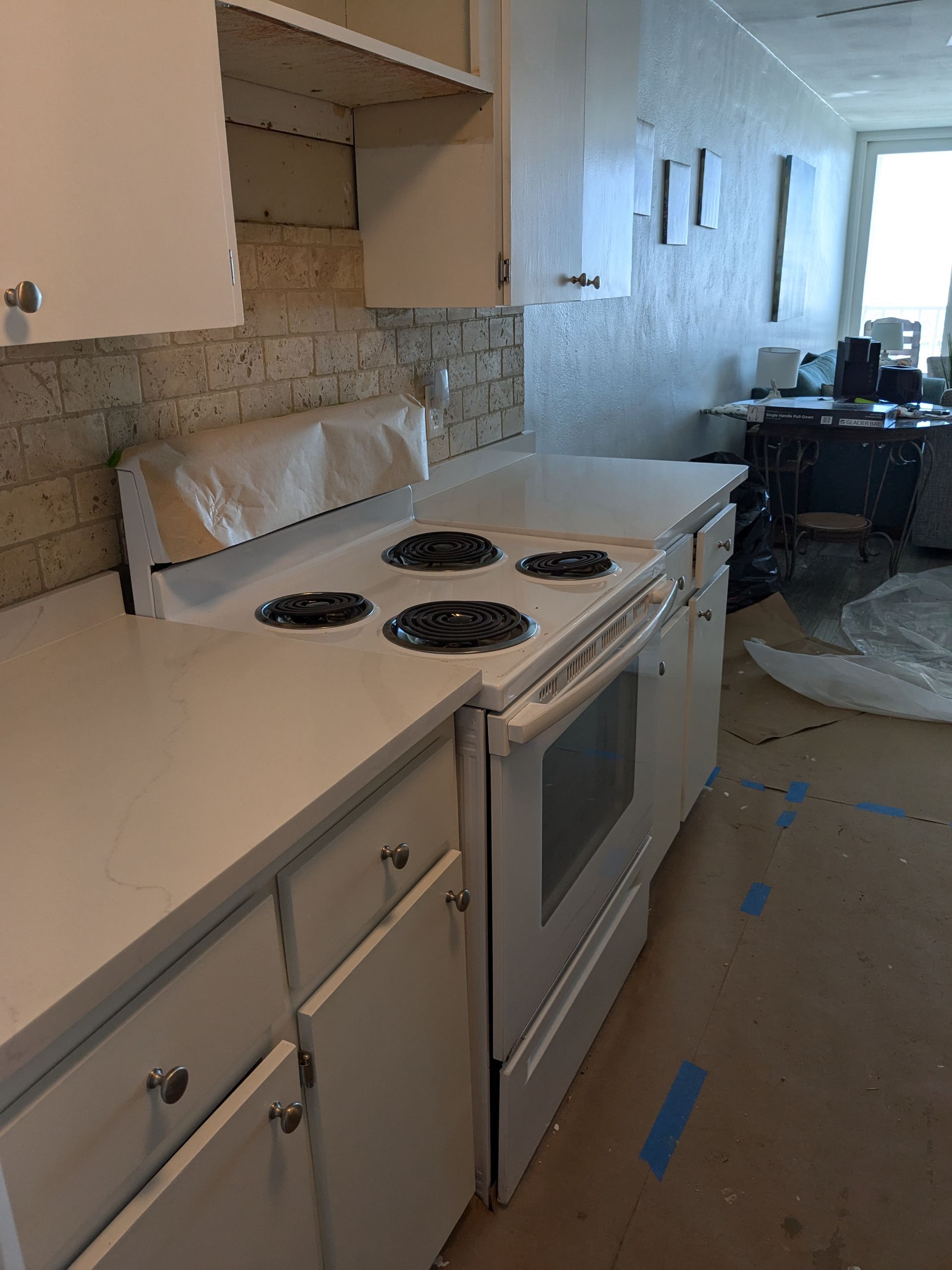 White kitchen with a stove, cabinets, and a counter with a tile backsplash.