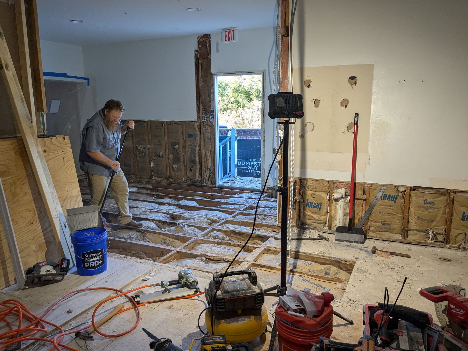Man demolishing a room.  Exposed walls and flooring.  Construction tools are visible.