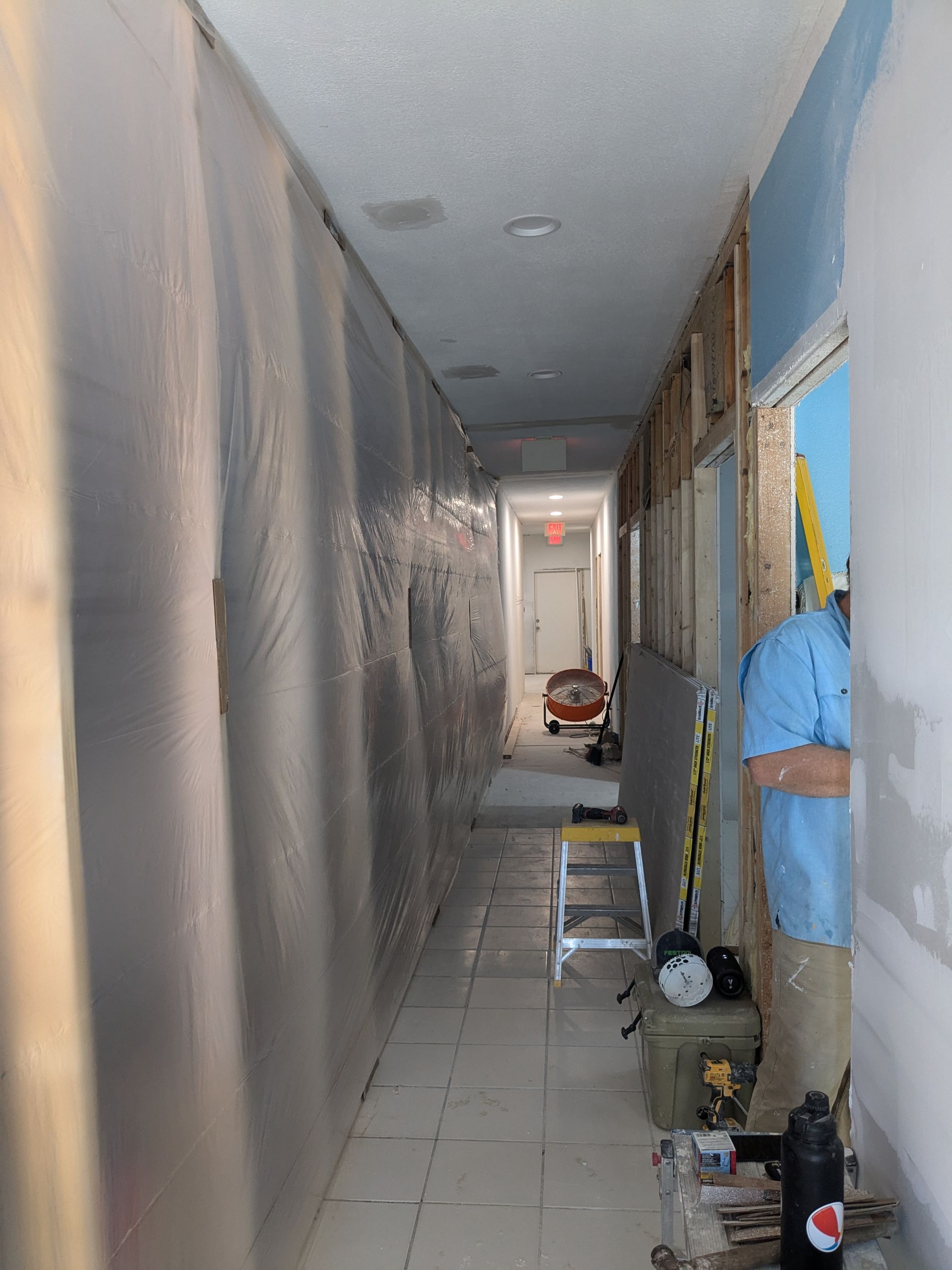 Long hallway under construction with plastic sheeting, doorway, and tools.