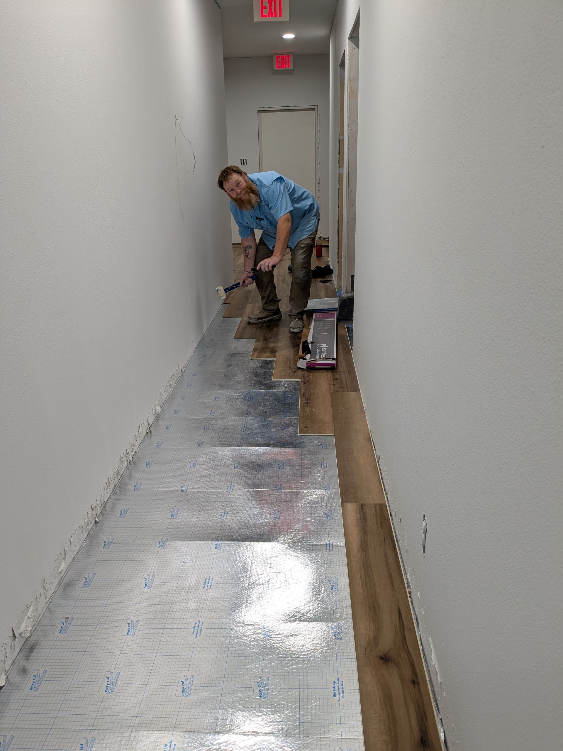 Man installing wood flooring in a narrow hallway, using a hammer.