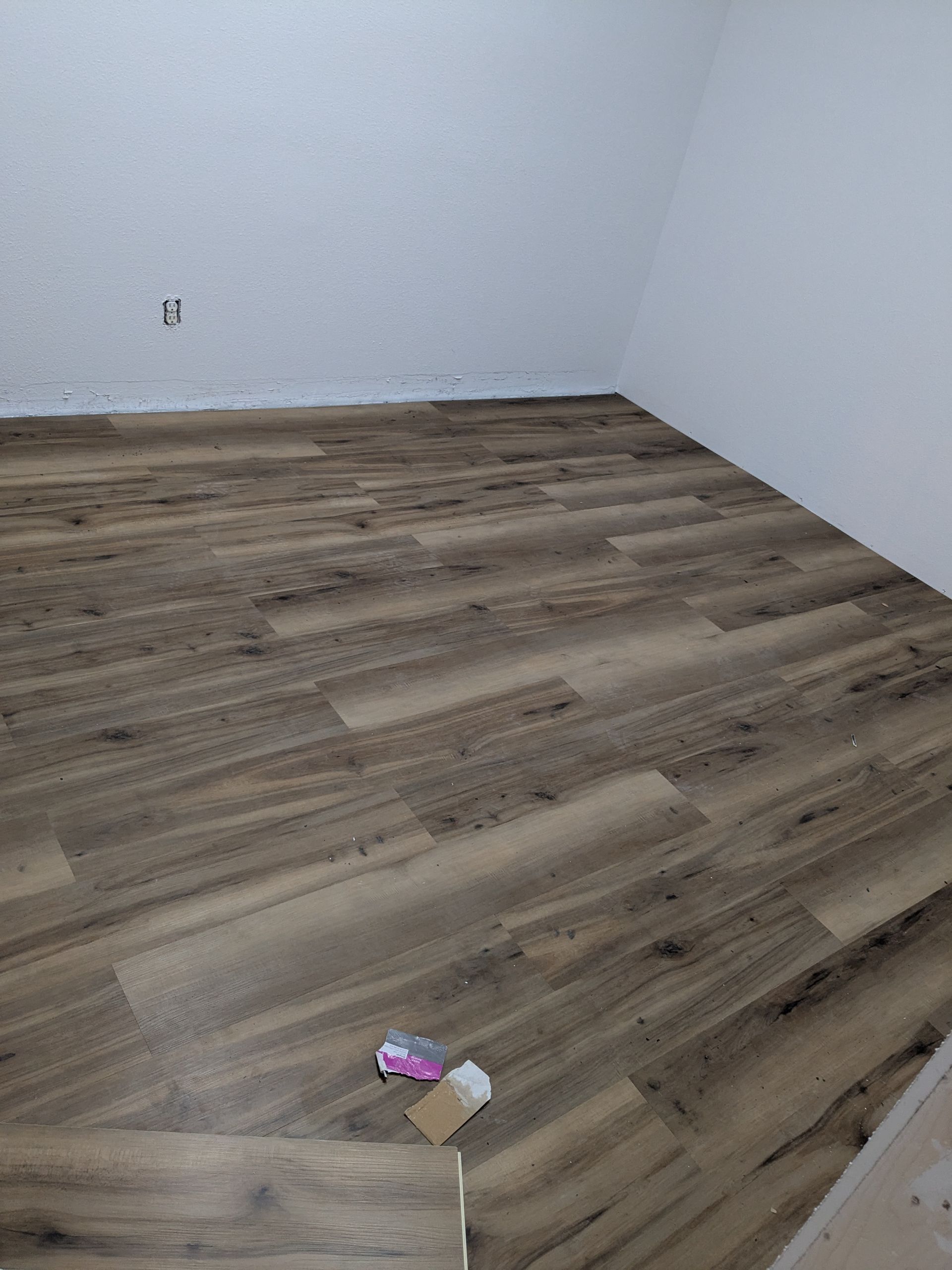 Room with wood-look flooring installed; walls are white. Debris on floor.