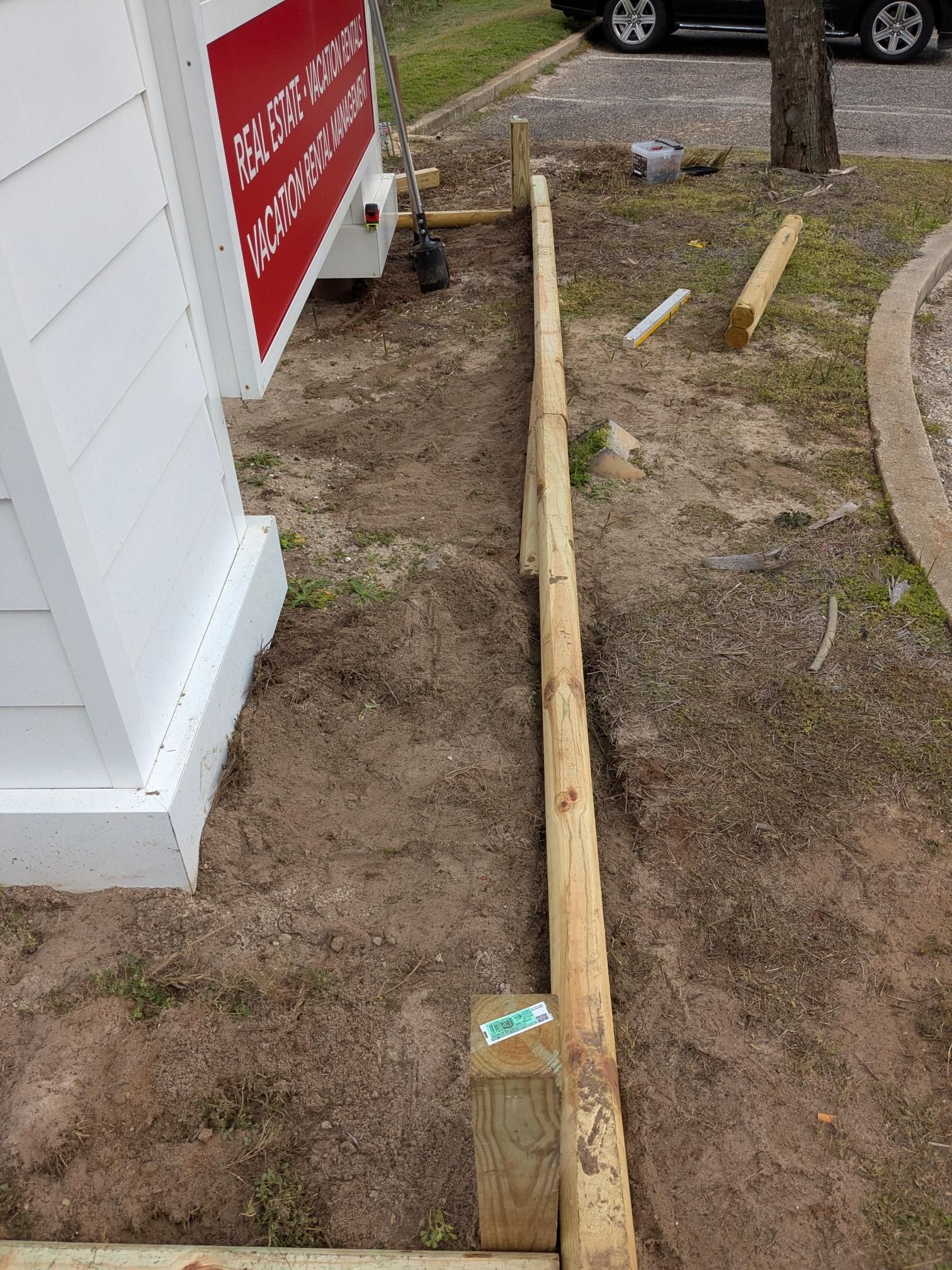 Construction site: wooden beams laid on the ground, likely for a fence, next to a white building.
