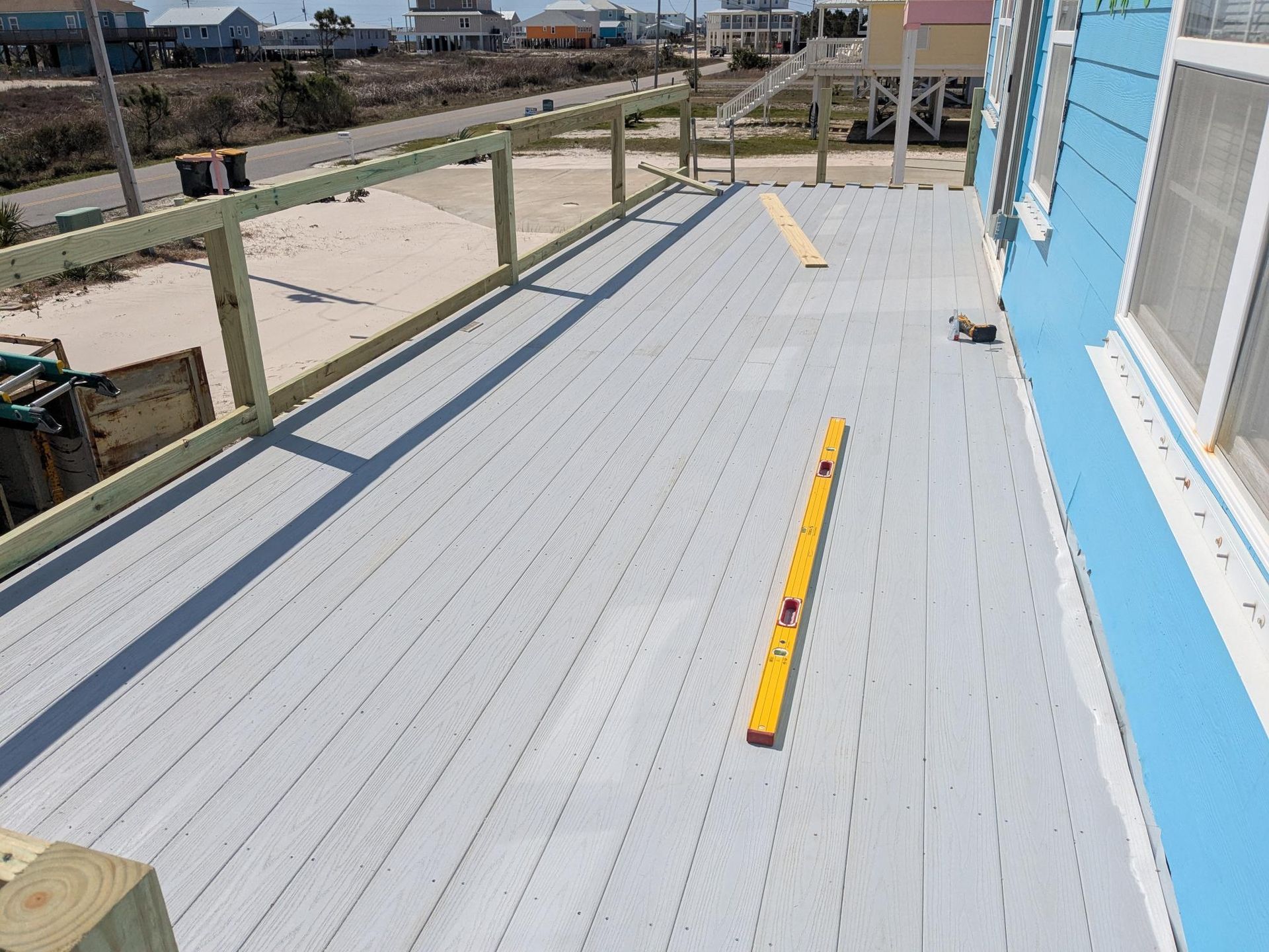 A light gray deck with wooden railing and level. Blue house on right, road and houses in the background.