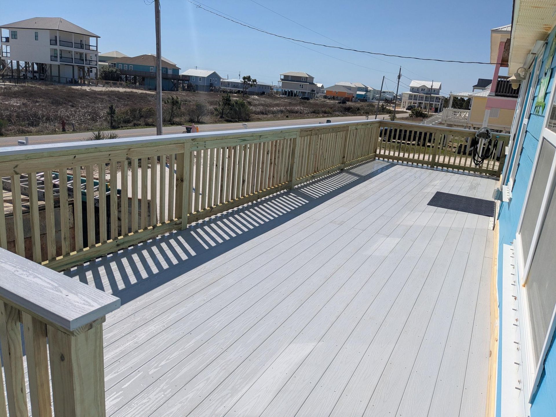 Large outdoor deck with gray decking, light wood railing, and coastal homes in the background.