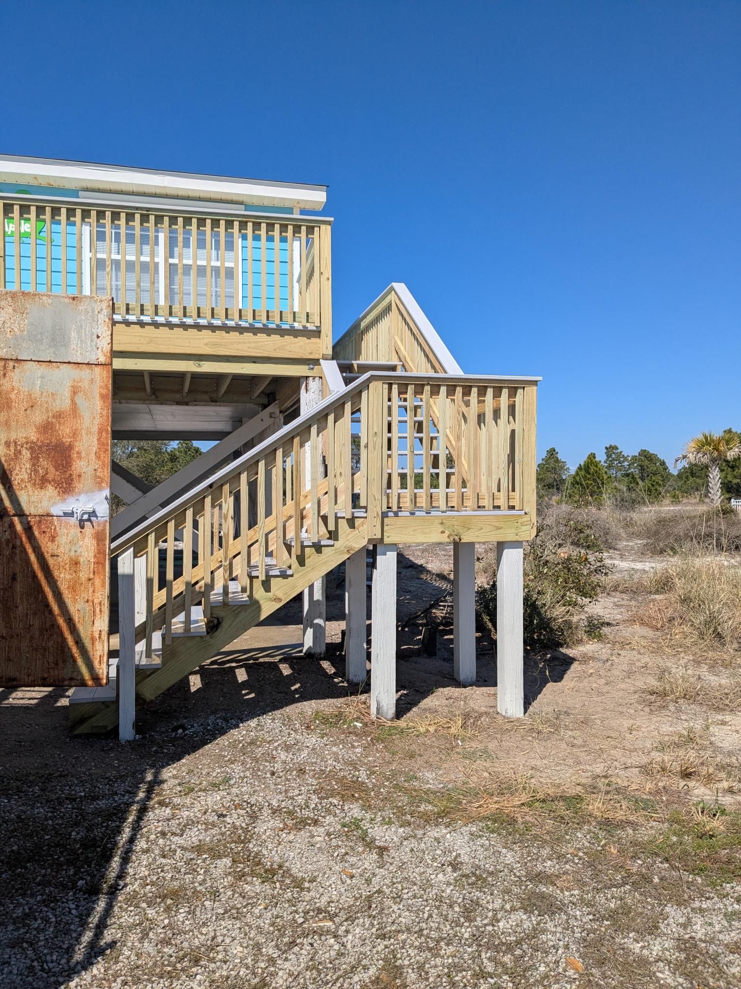 Wooden elevated structure with stairs and light blue accents under a clear blue sky.