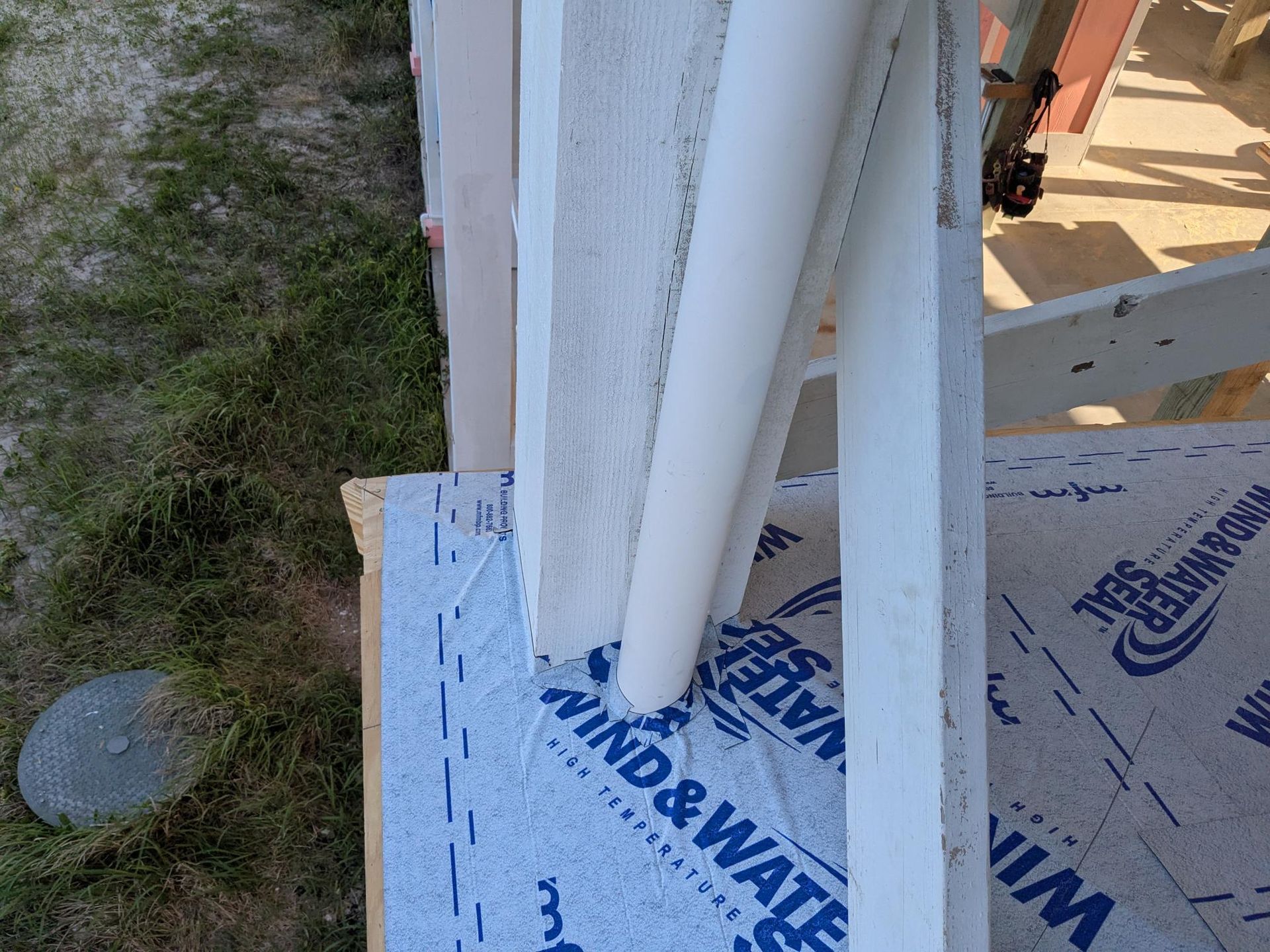Construction site: white pipes and protective wrap over blue waterproof barrier on a partially built structure.
