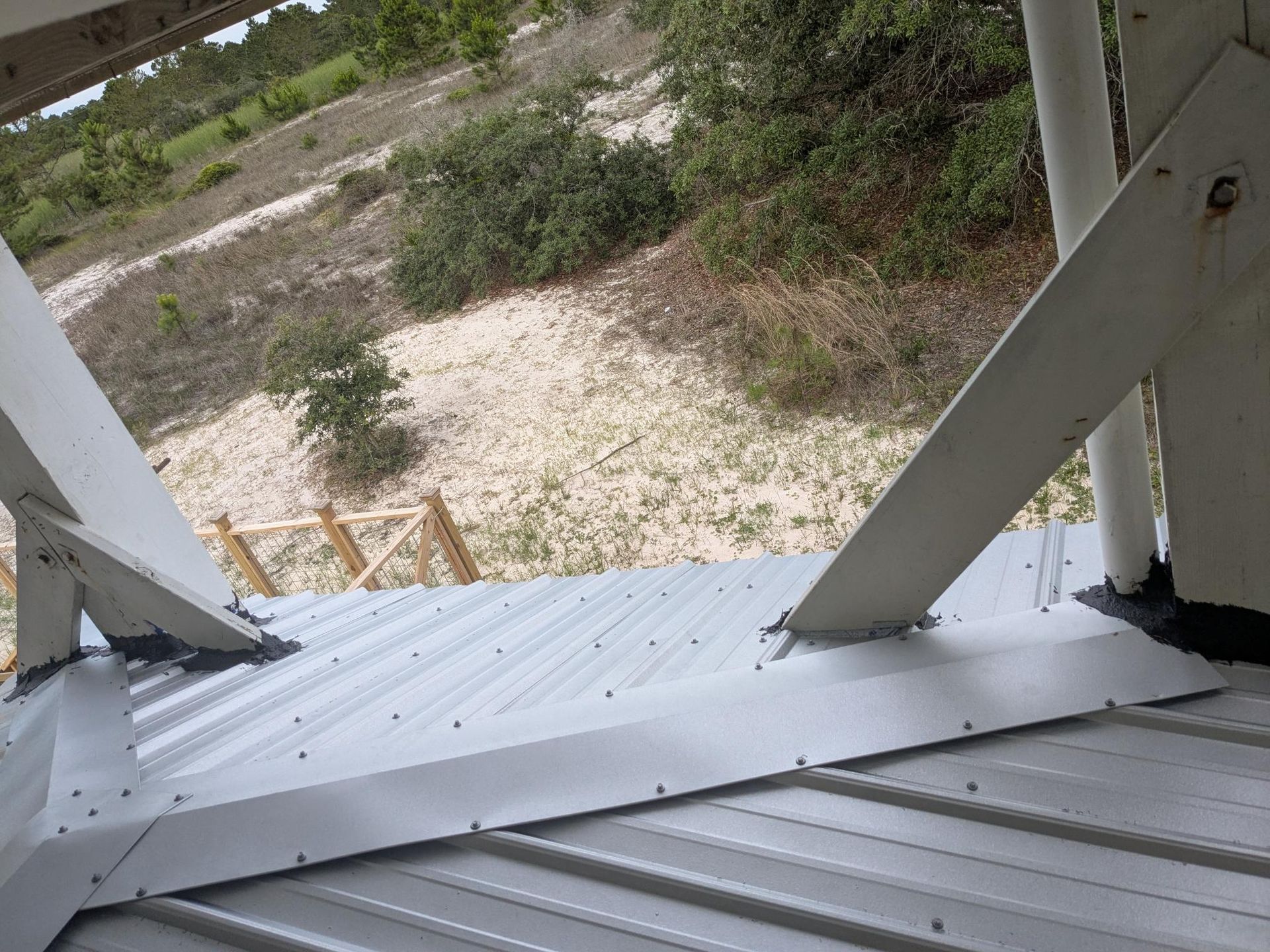 Metal roof structure with angled beams; view of landscape beyond.