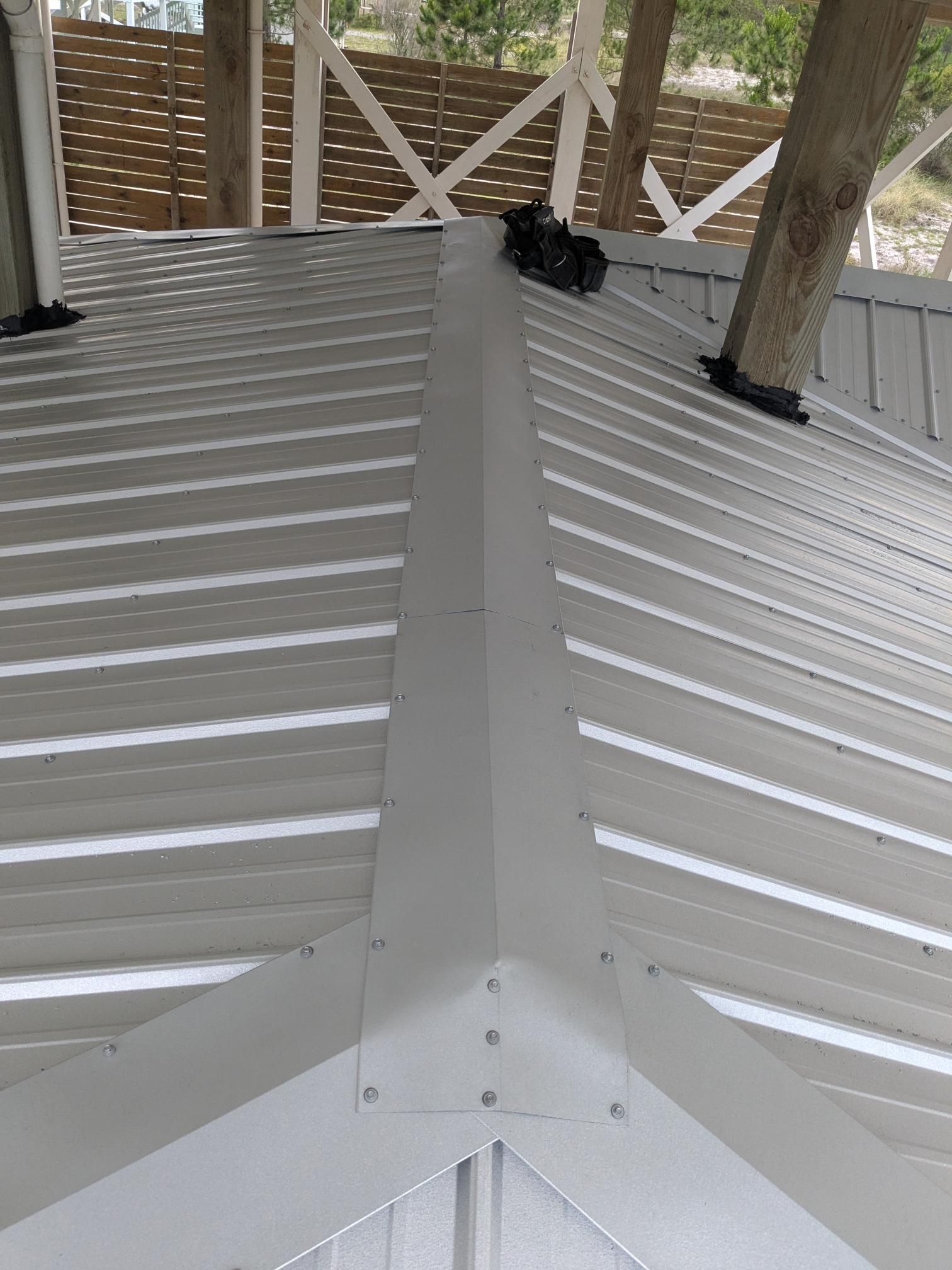 White metal roof with angled ridges, corner joints, and a tree trunk.