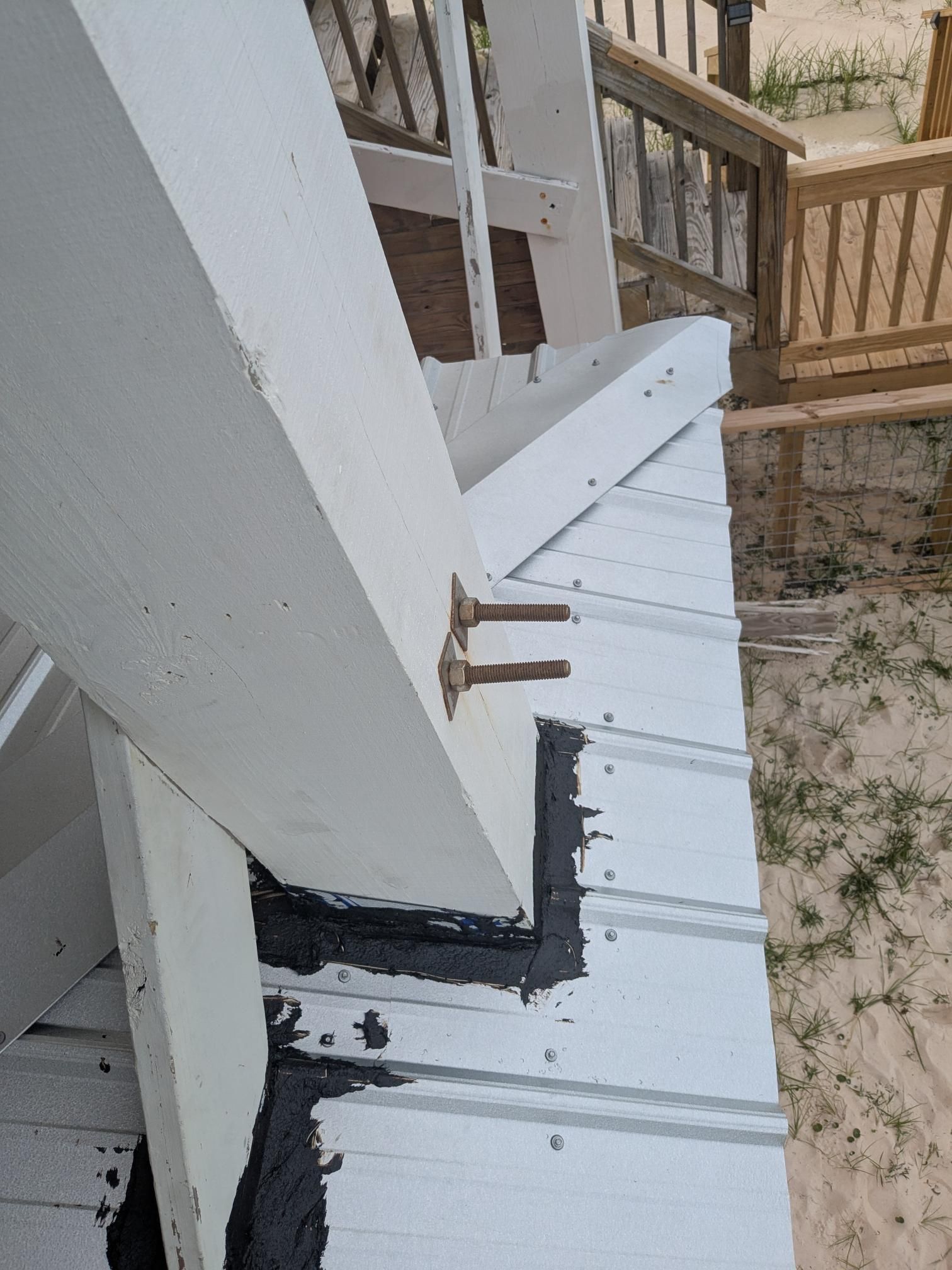 White wooden structure with metal hardware attached to a white corrugated metal roof. Black sealant is visible.