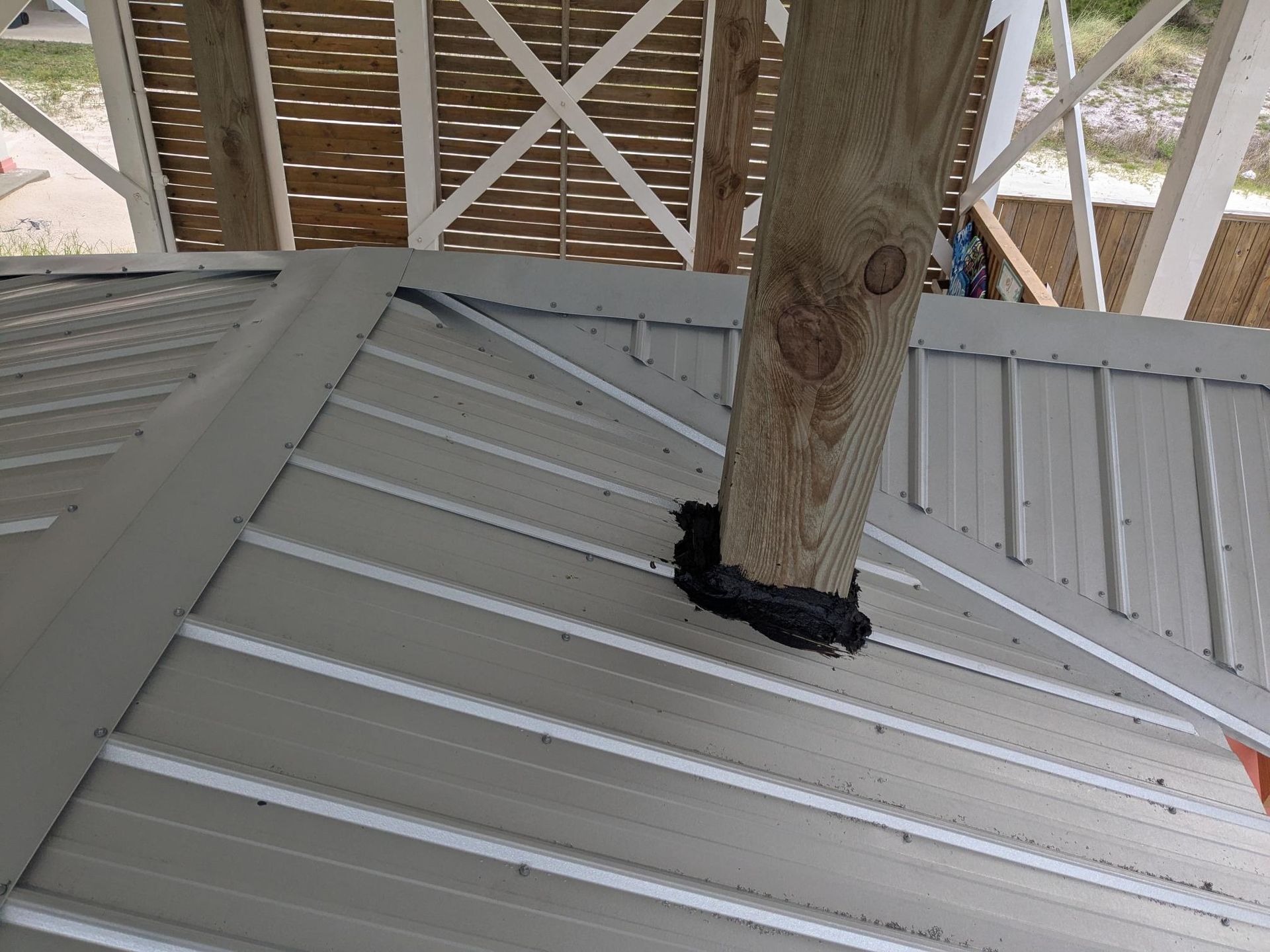 Metal roof with a wooden post sealed with black caulk; part of a gazebo.