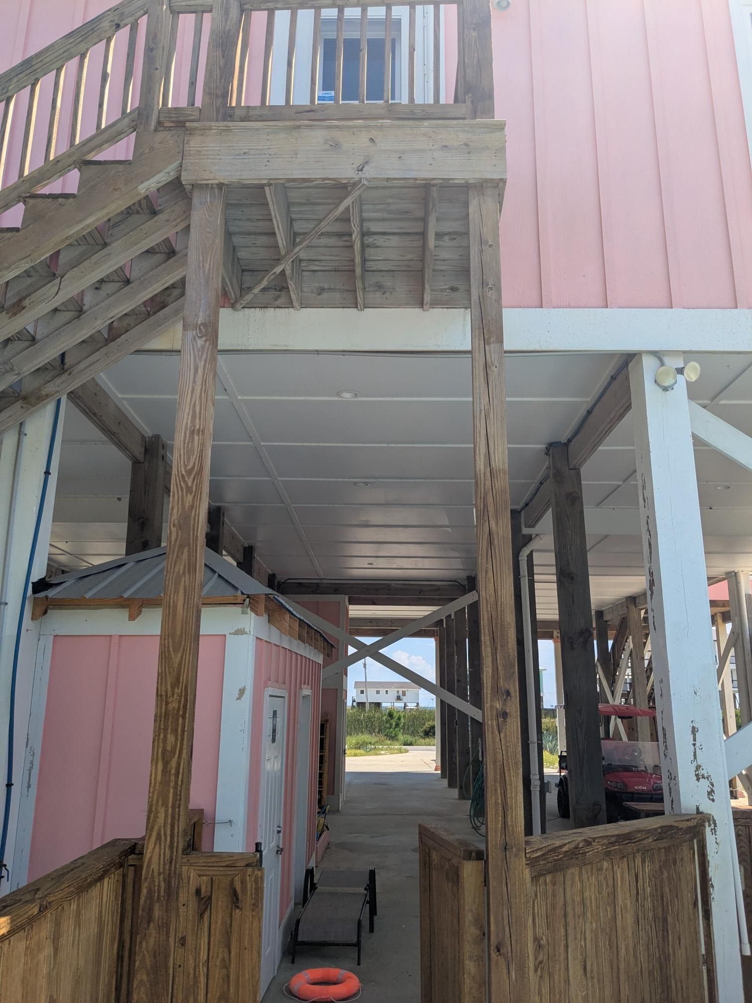 Stairs and walkway under a raised building. Pink and white building with a wooden staircase and support beams.
