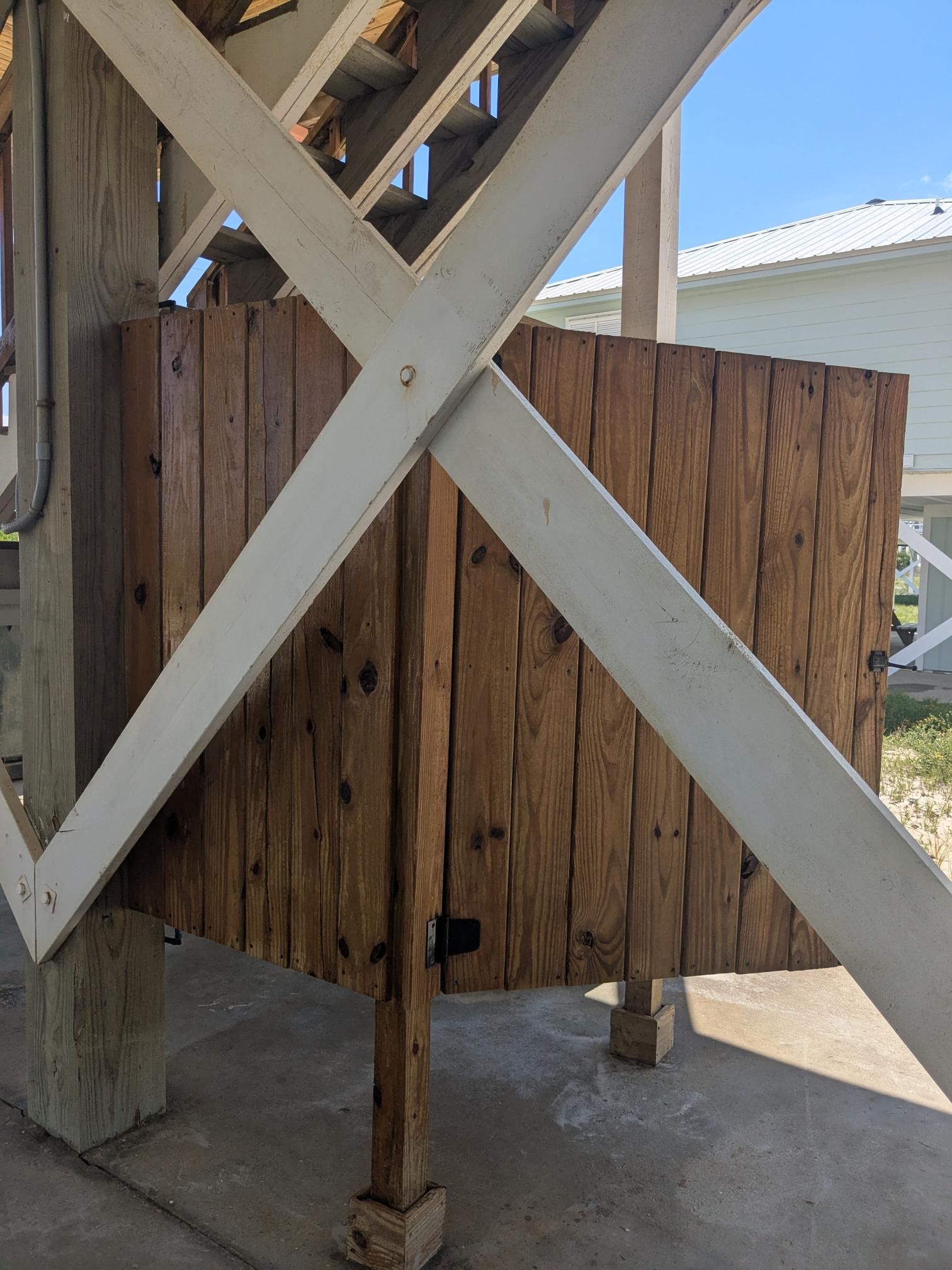 Wooden outdoor shower on a raised deck, supported by white beams.
