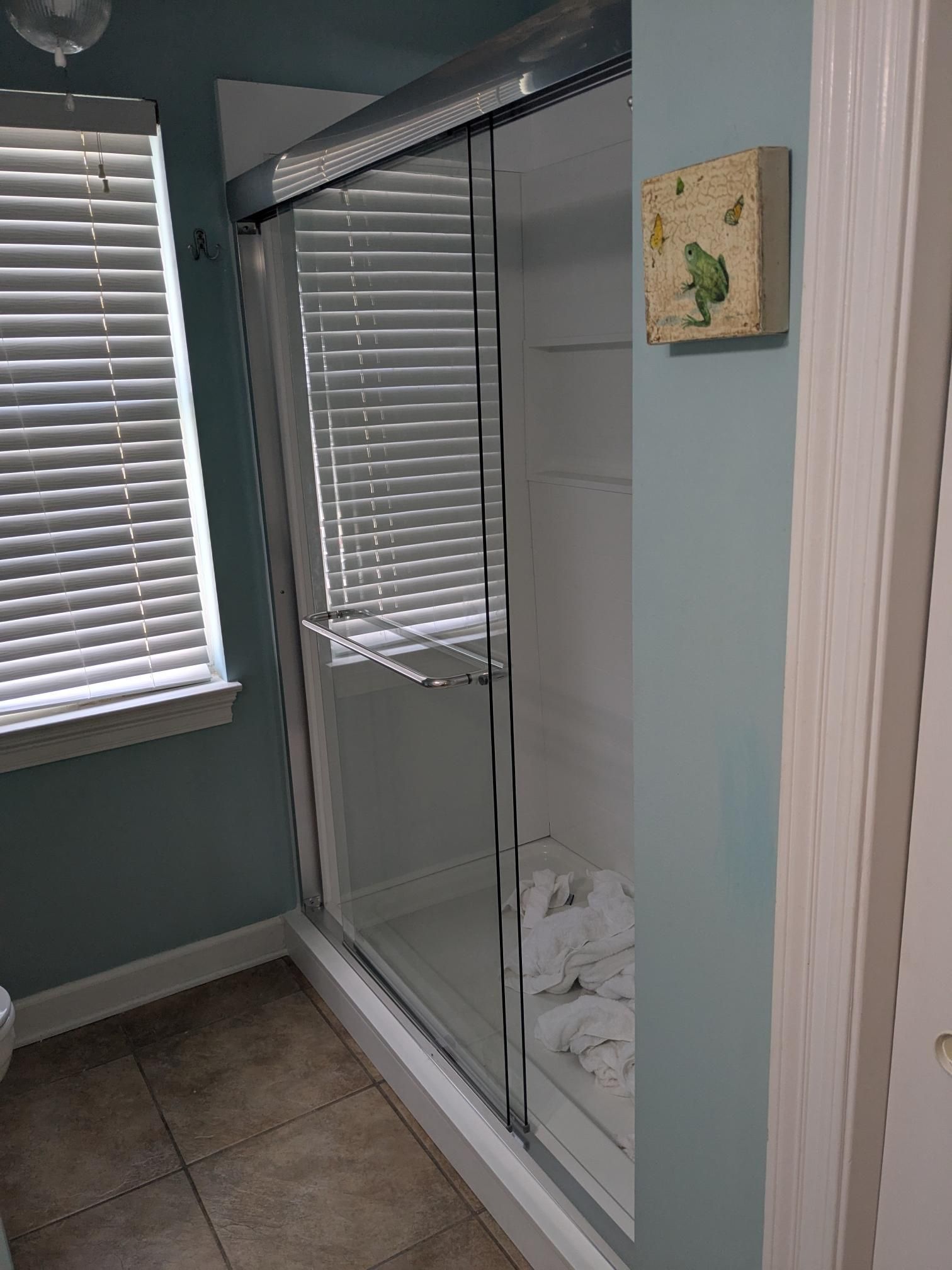 Bathroom with a glass shower, closed blinds, and blue walls.