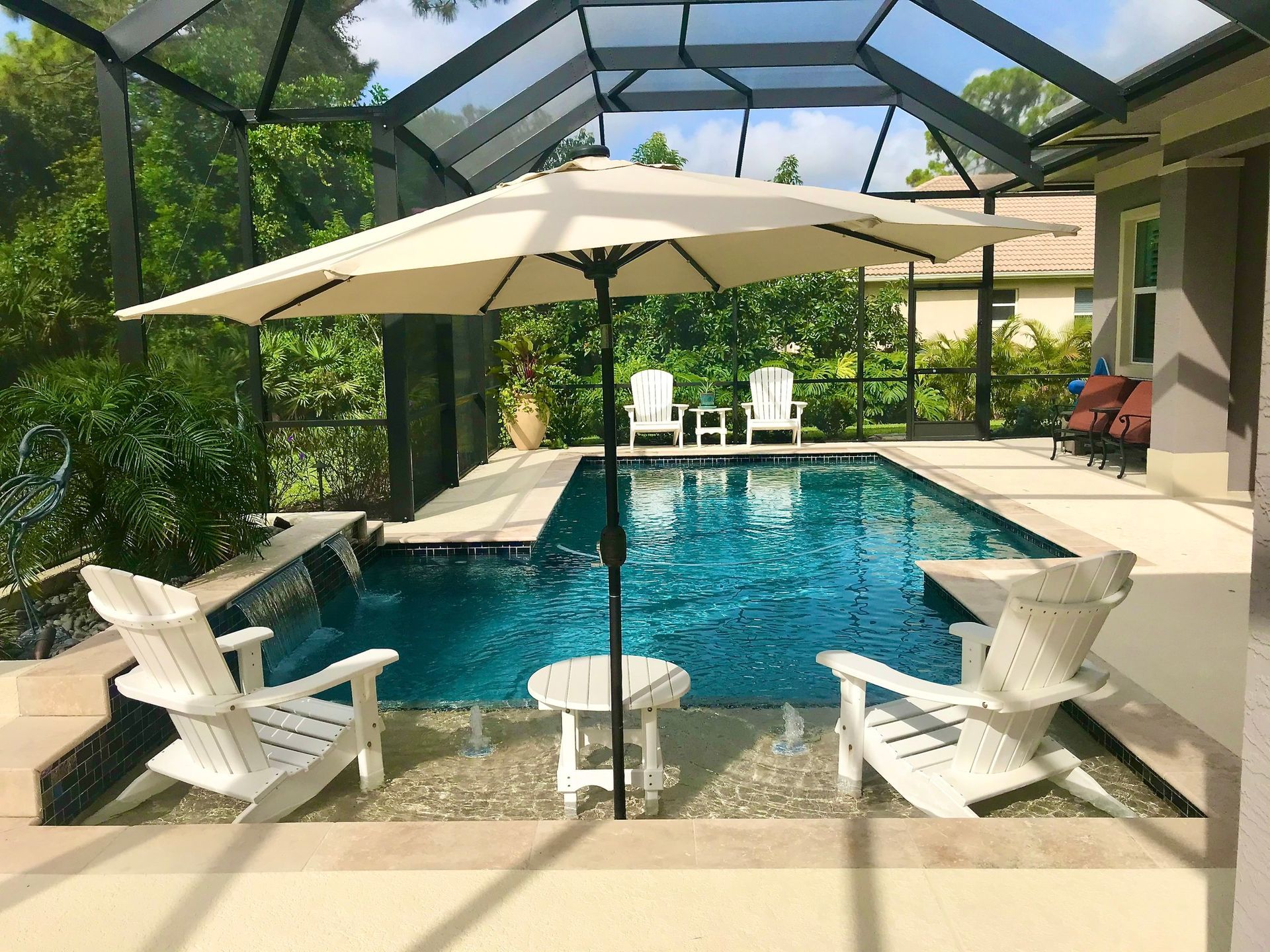 A swimming pool with chairs and an umbrella under a screened in area.