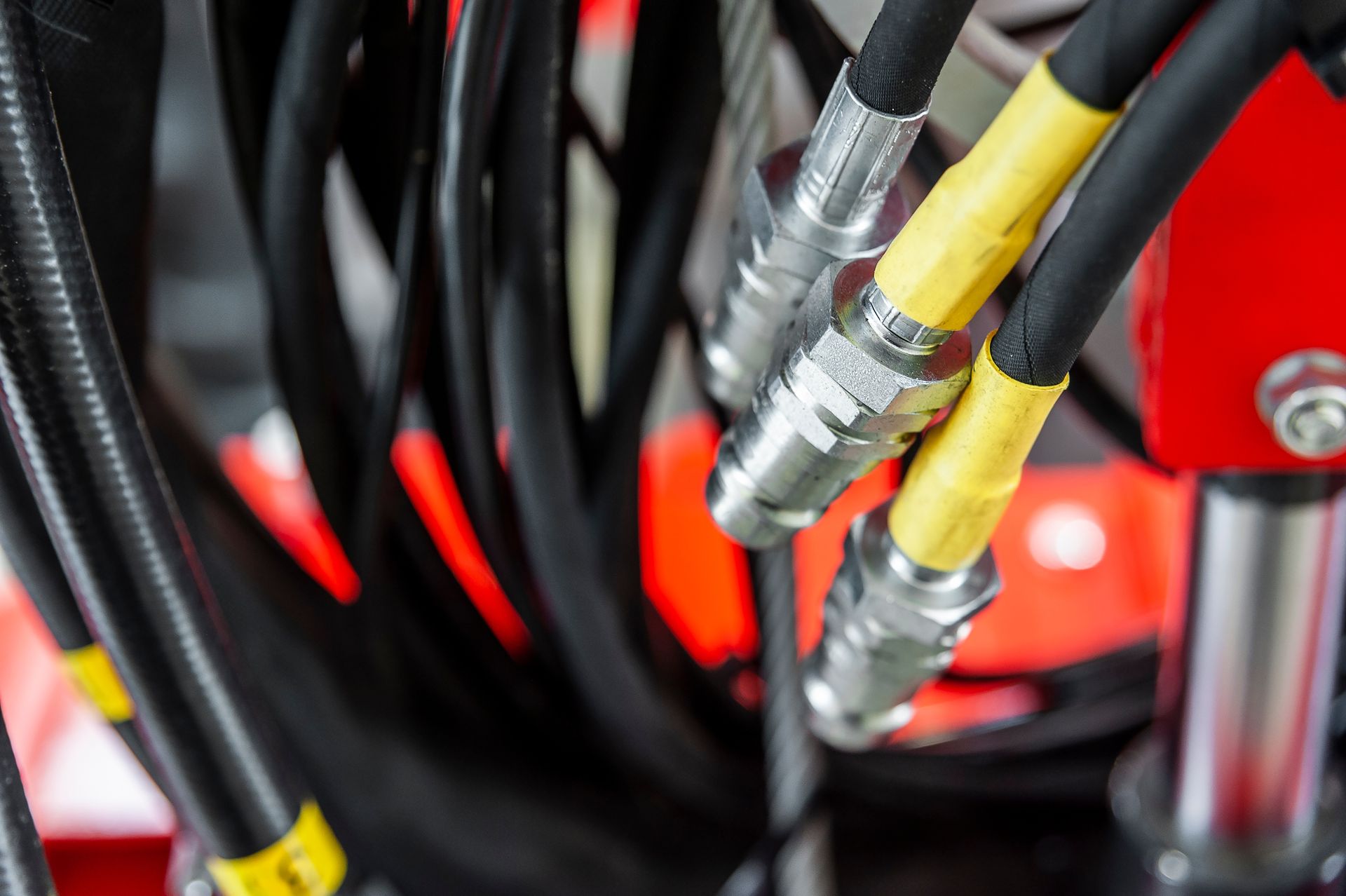 Close-up of hydraulic hoses with metal fittings connected to industrial machinery.