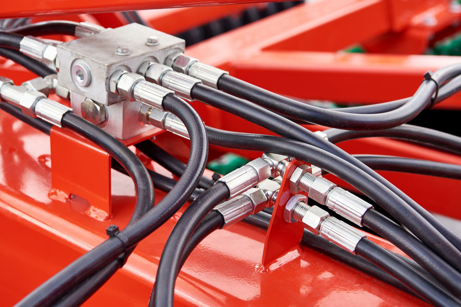 Close-up of hydraulic hoses and metal fittings on red industrial machinery. Close-up of hydraulic hoses and metal fittings on red industrial machinery.