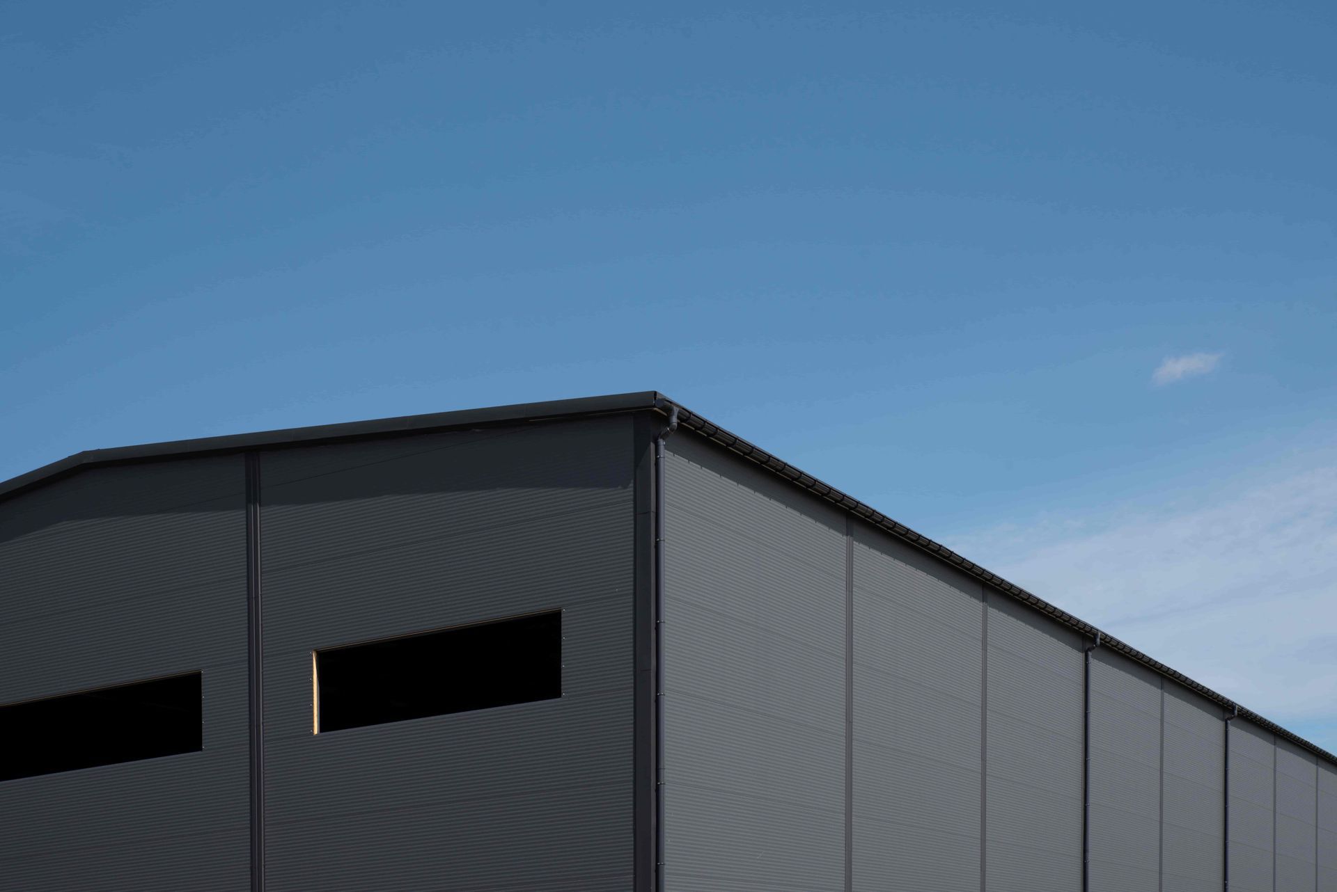Gray industrial warehouse under a clear blue sky with dark horizontal windows