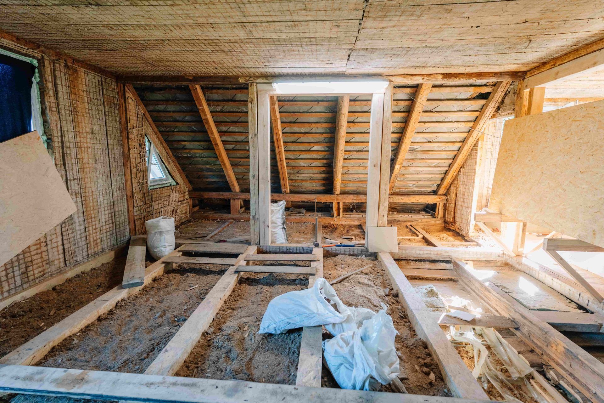 Attic under renovation with exposed wooden framing, insulation, and construction materials on the floor