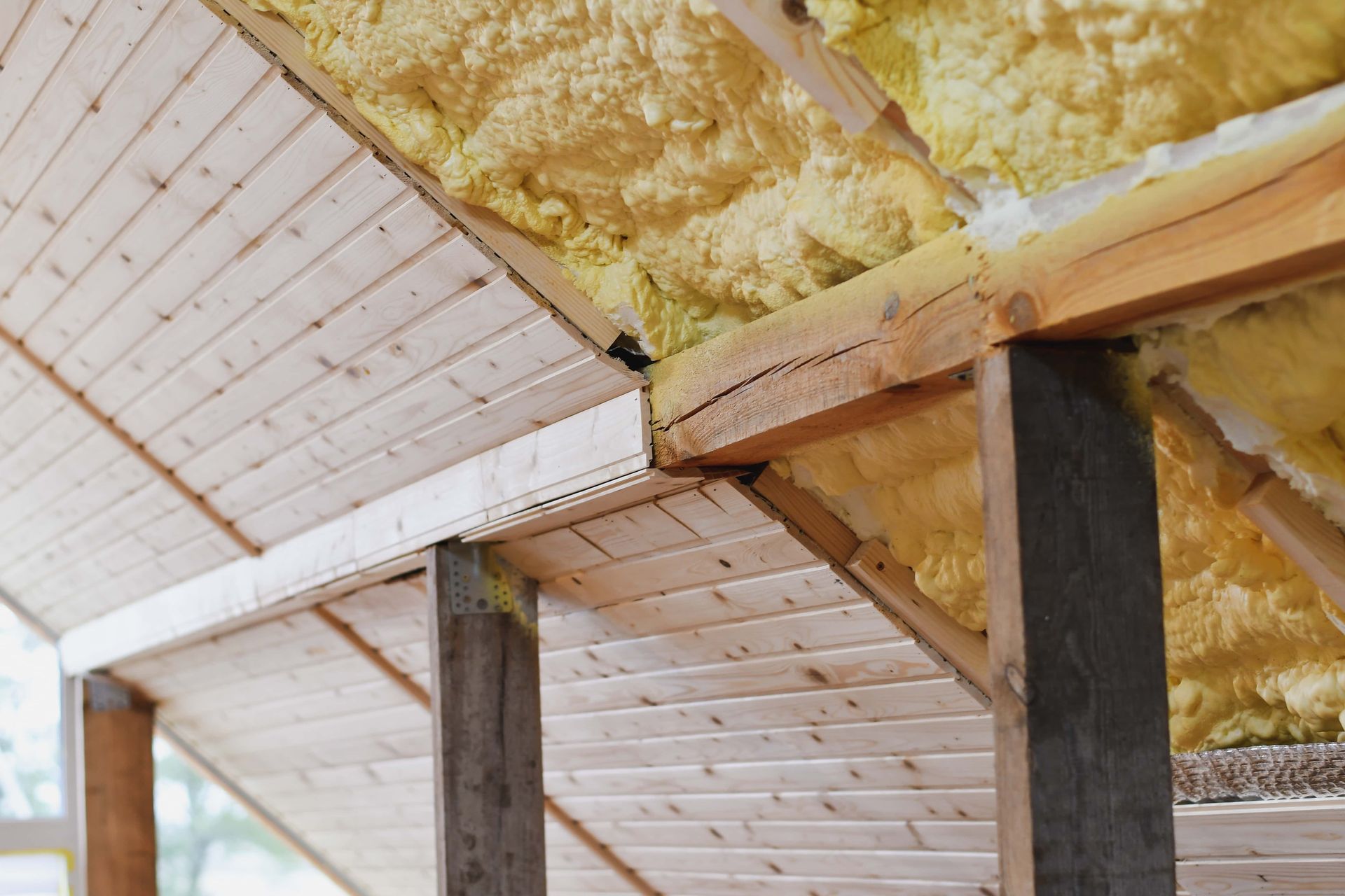 Close-up of insulated roof joists with yellow fiberglass and white paneling inside an unfinished attic