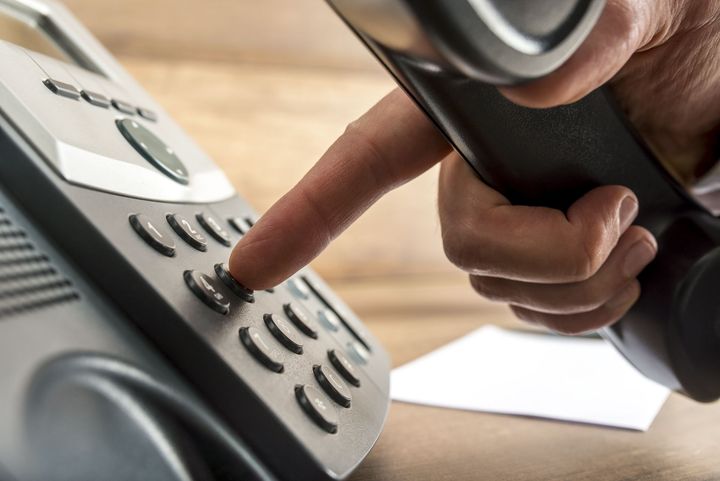Finger pressing a button on a gray office desk phone close-up