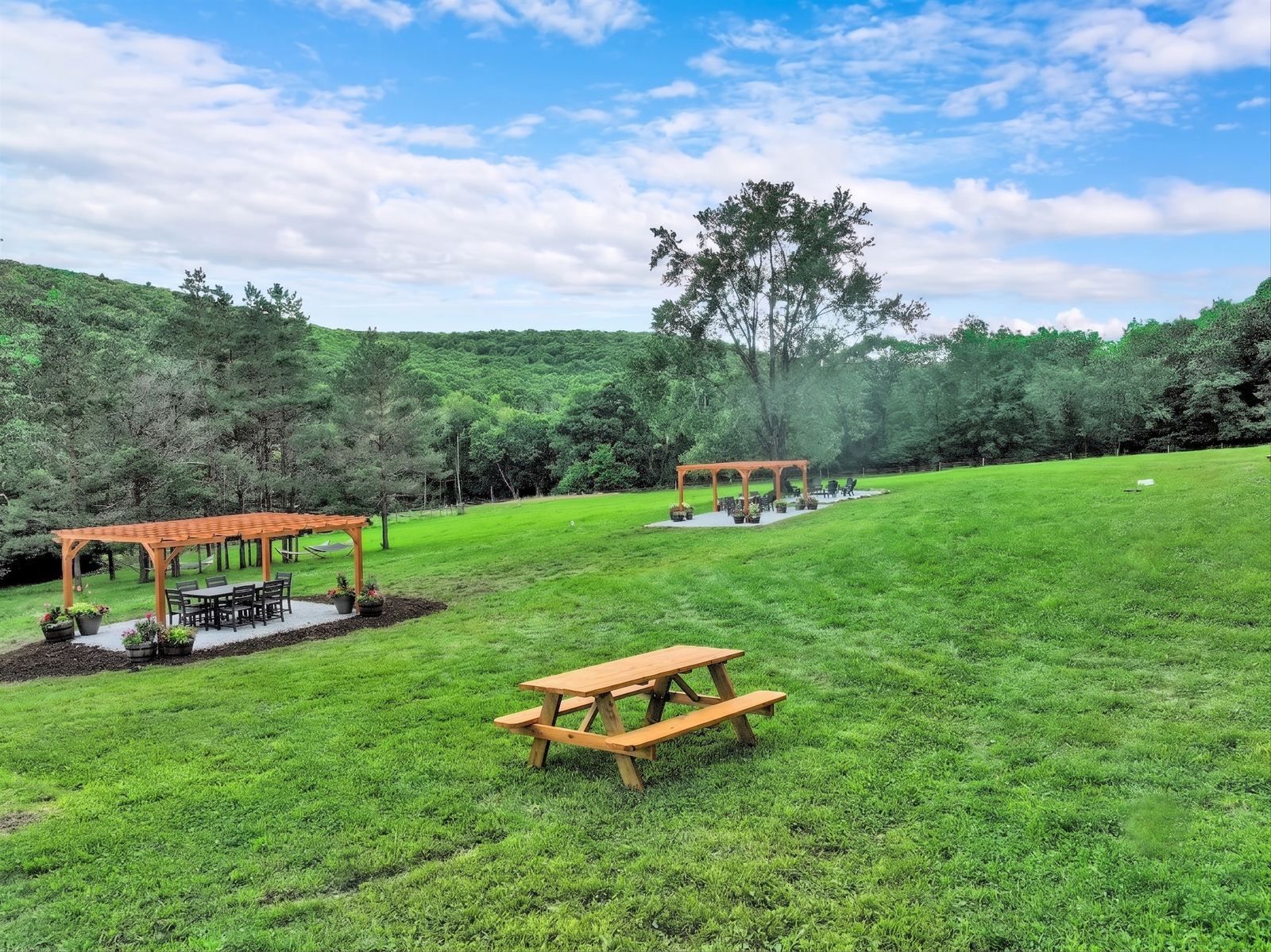 Green summer lawn with a pergola, picnic tables and mountains beyond