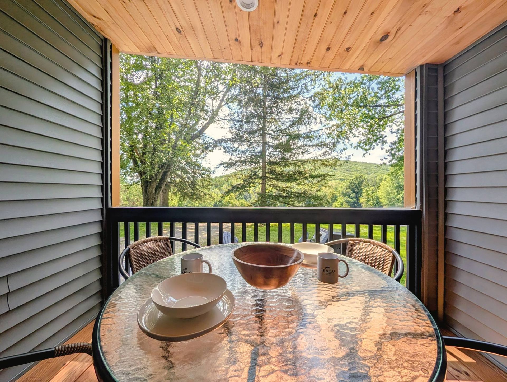 Covered porch table with Ik & Lo mugs, looking out to trees and hills