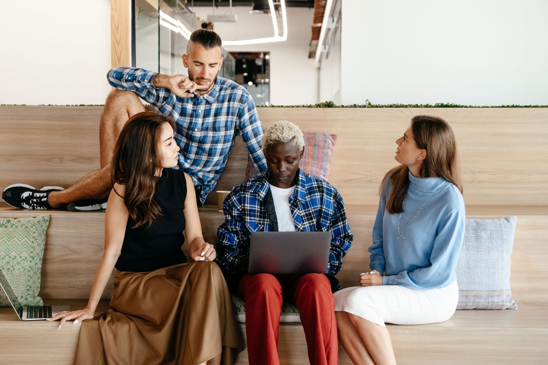 Group of people in an informal workplace setting having a conversation. One person is using a laptop.