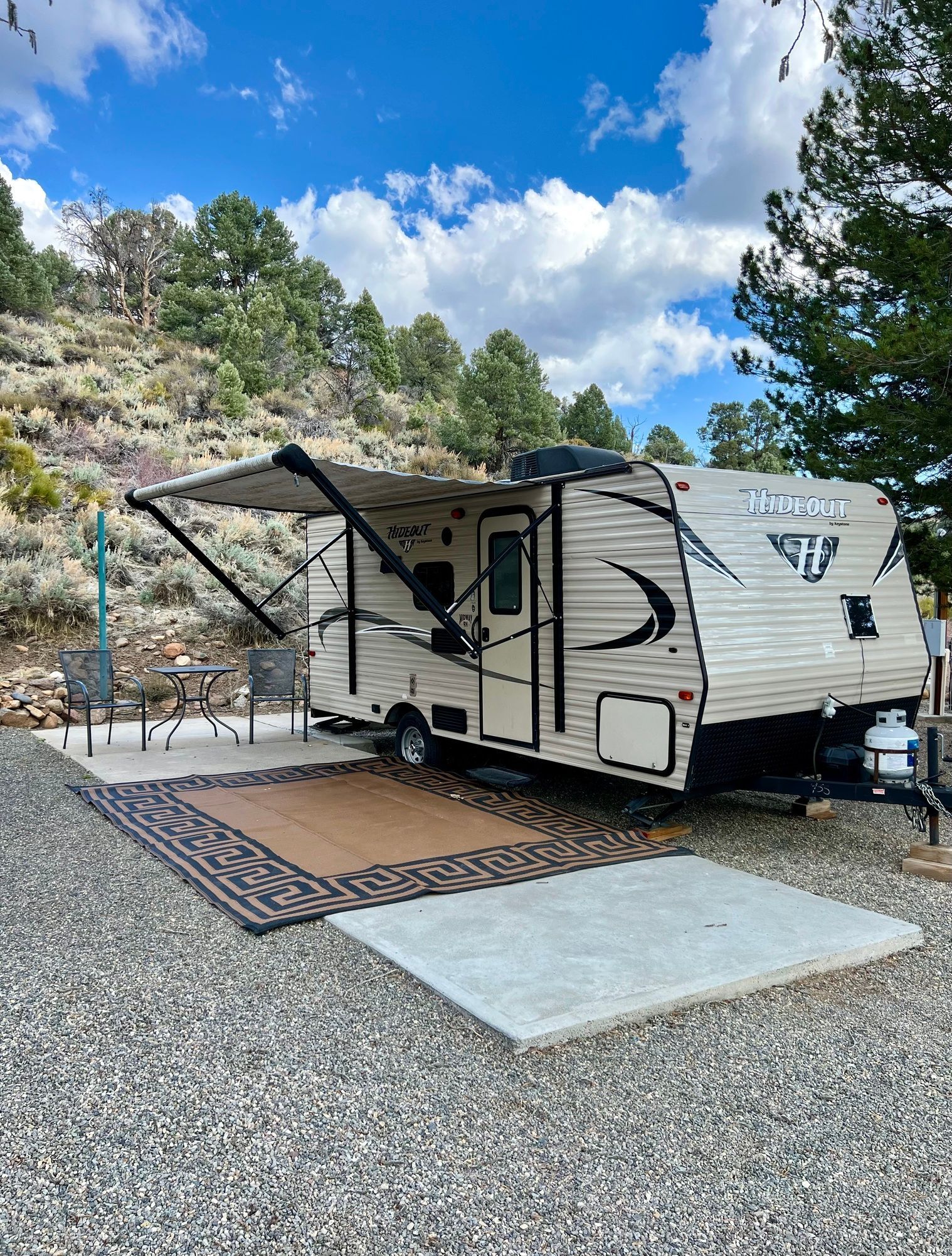 A rv is parked in a gravel lot with trees in the background.