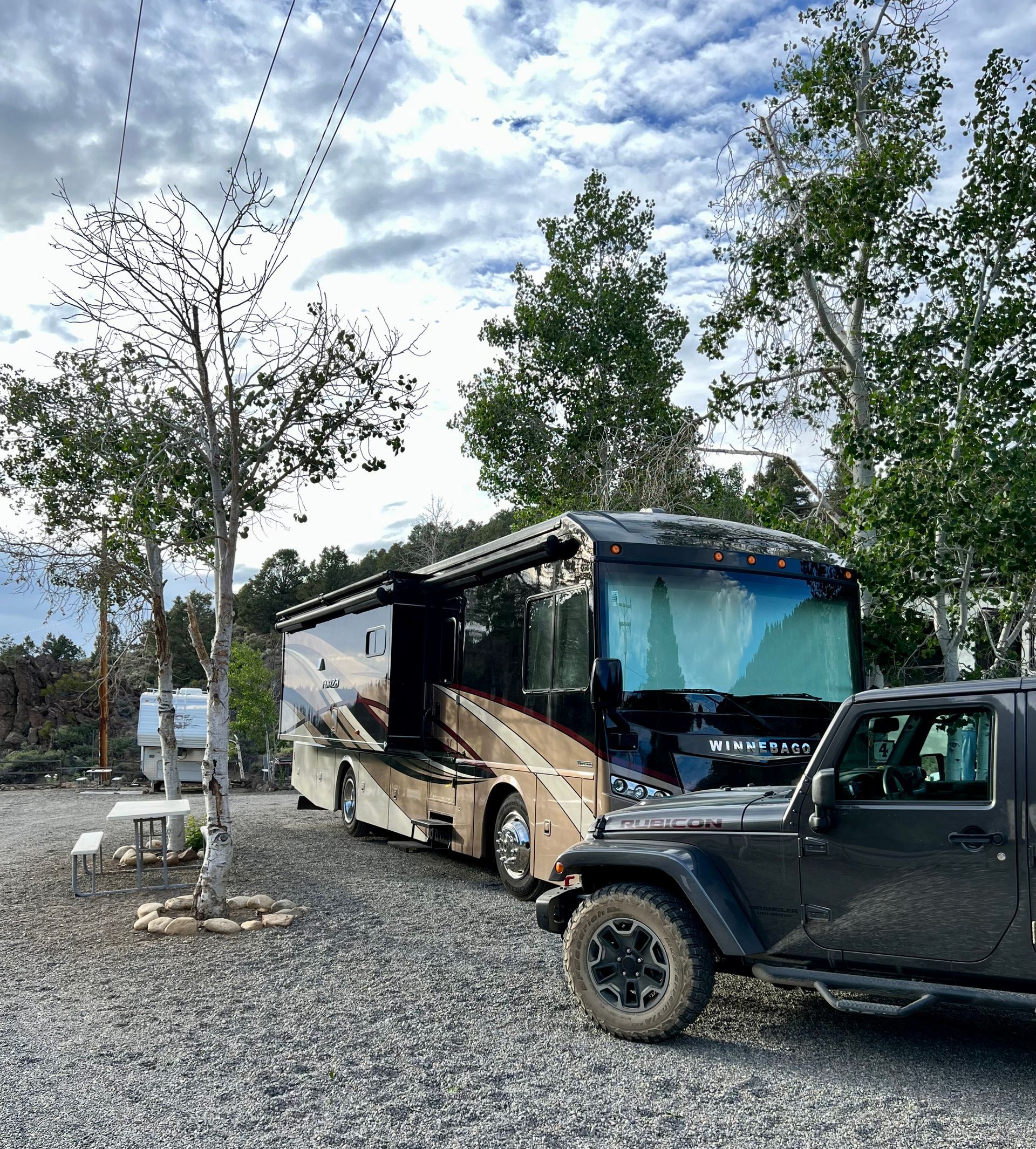 A jeep is parked next to a rv in a gravel lot.