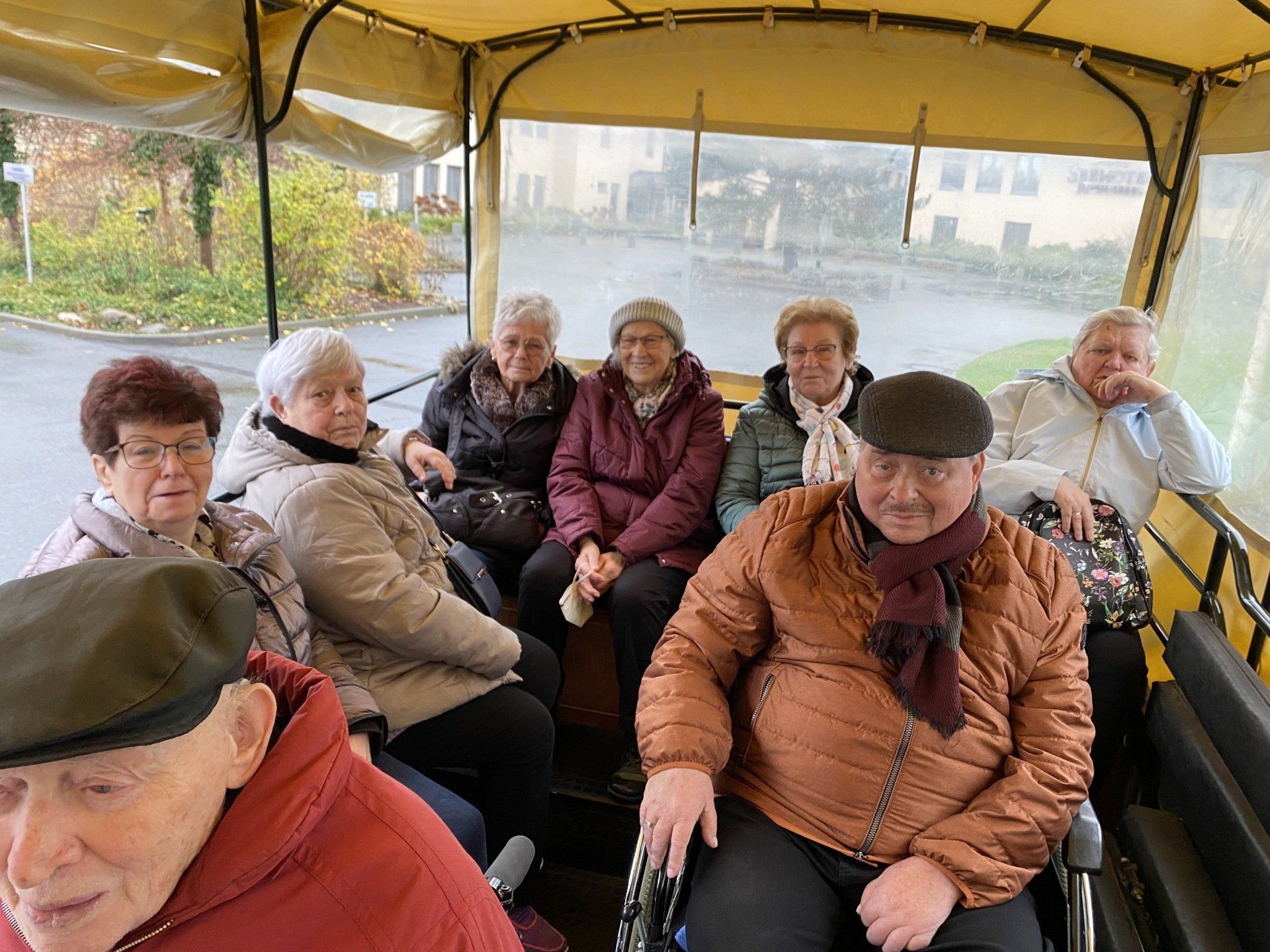 Gruppe von Menschen in einem Planwagen; lächelnd, legere Kleidung.