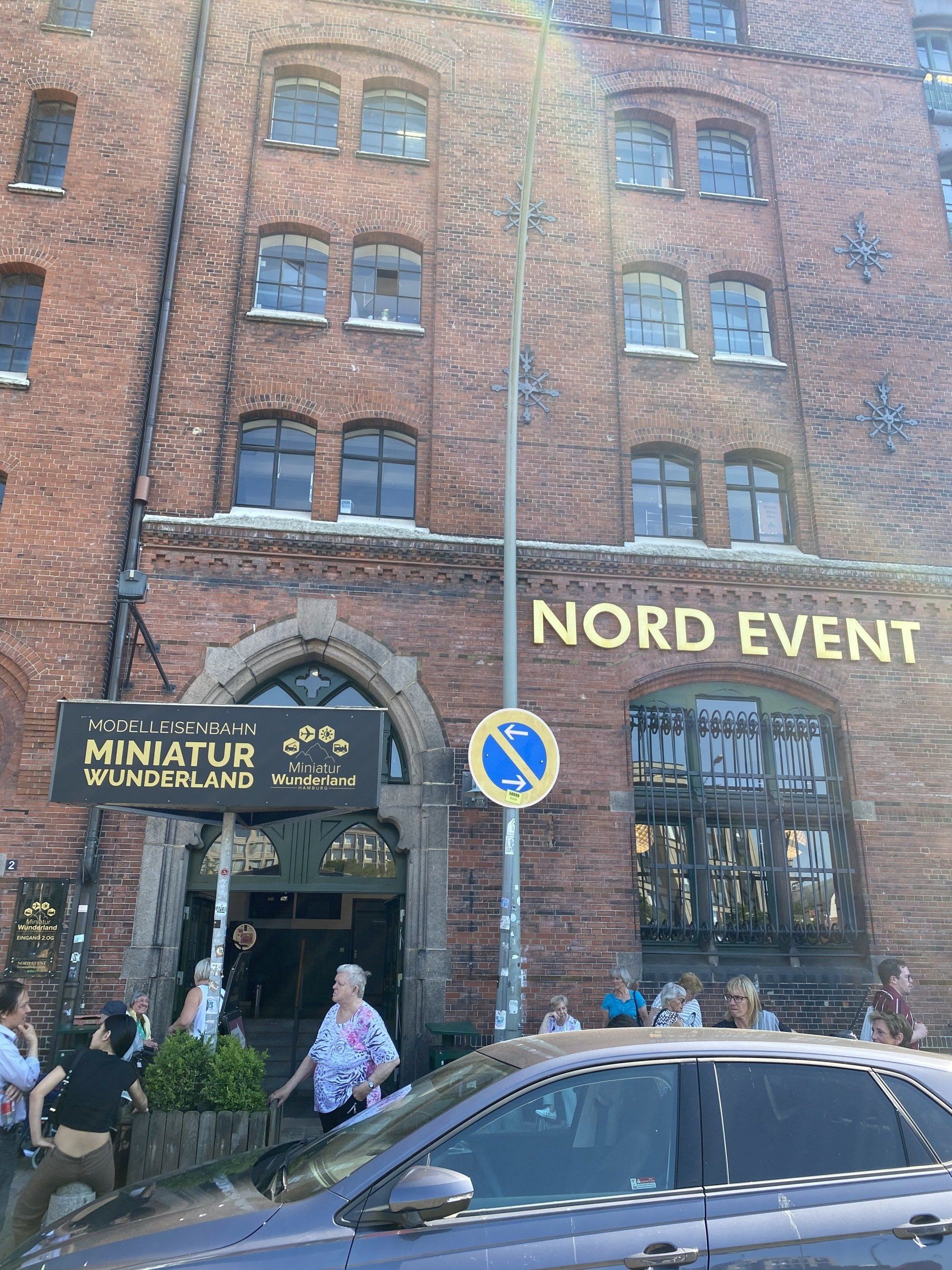 Eingang zum roten Backsteingebäude: Schild „Miniatur Wunderland“, darüber Schild „Nord Event“, Menschen, Auto.