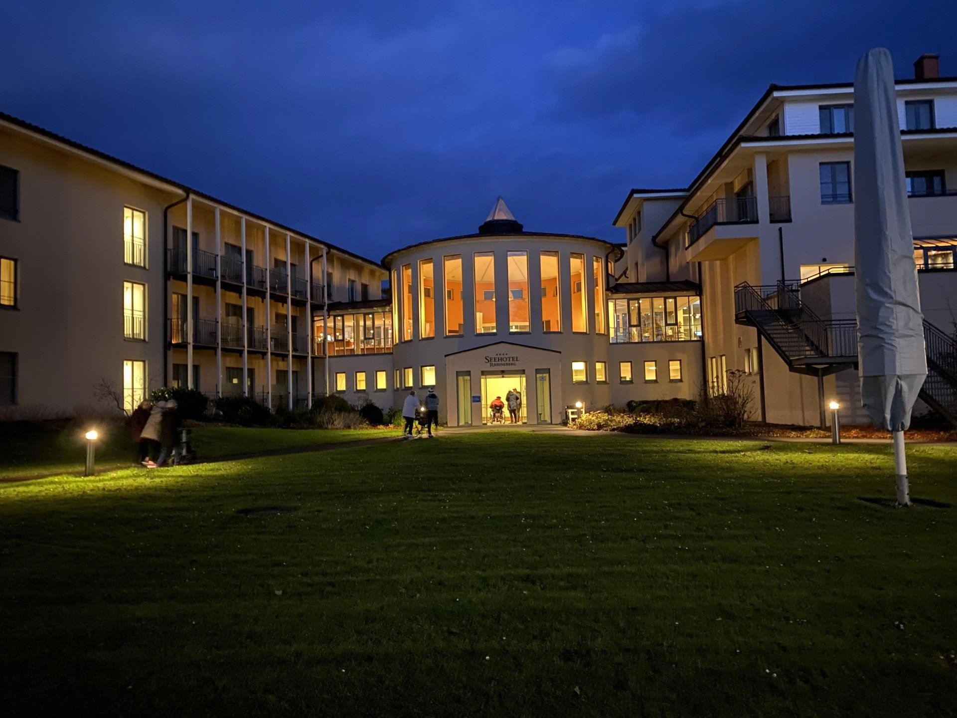 Außenansicht des Hotels bei Nacht mit beleuchteten Fenstern und einem kreisförmigen zentralen Gebäude auf einer Rasenfläche.