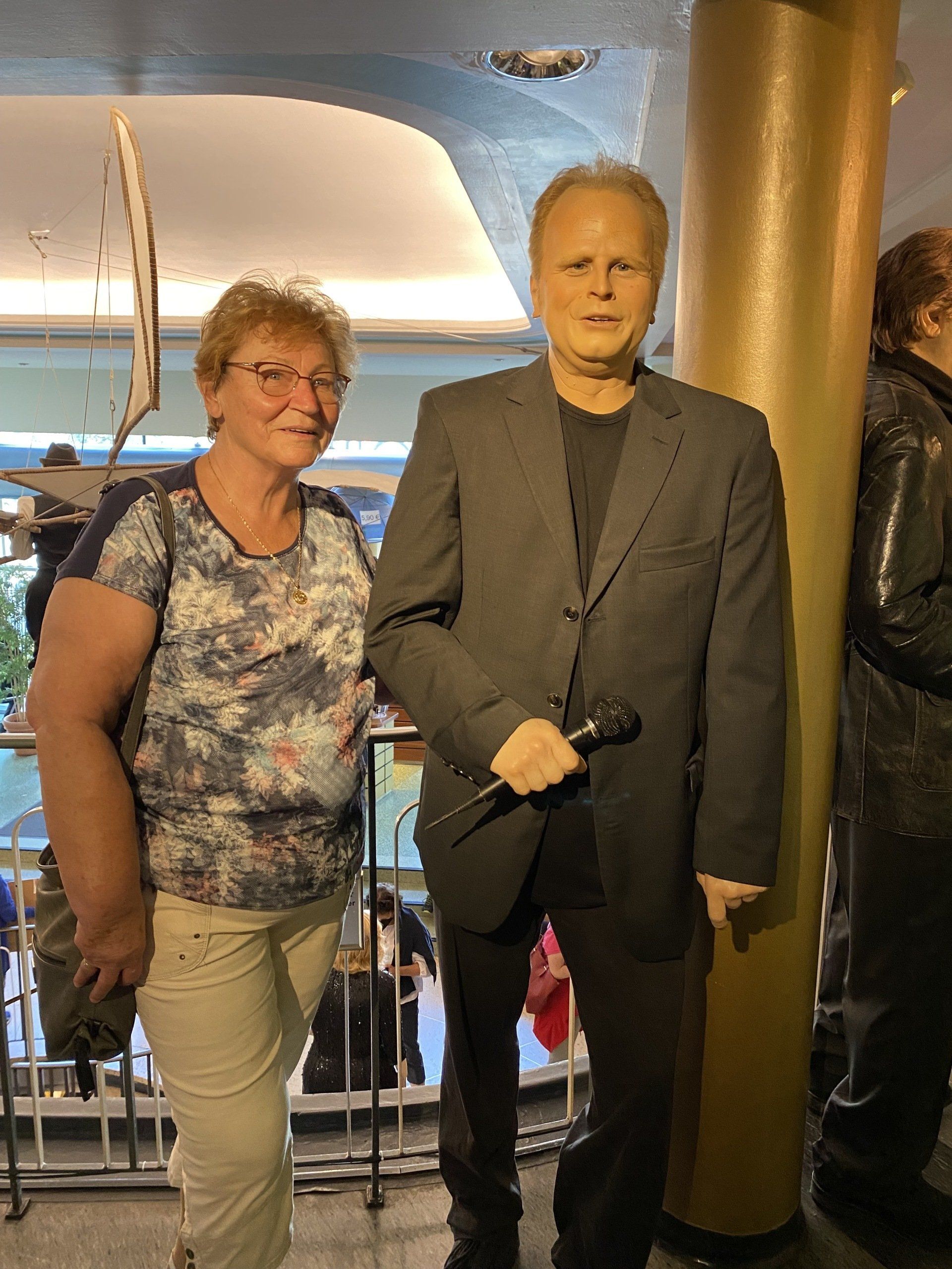 Frau posiert mit einer Wachsfigur einer Sängerin, die ein Mikrofon hält. Die Kulisse scheint ein Museum zu sein.