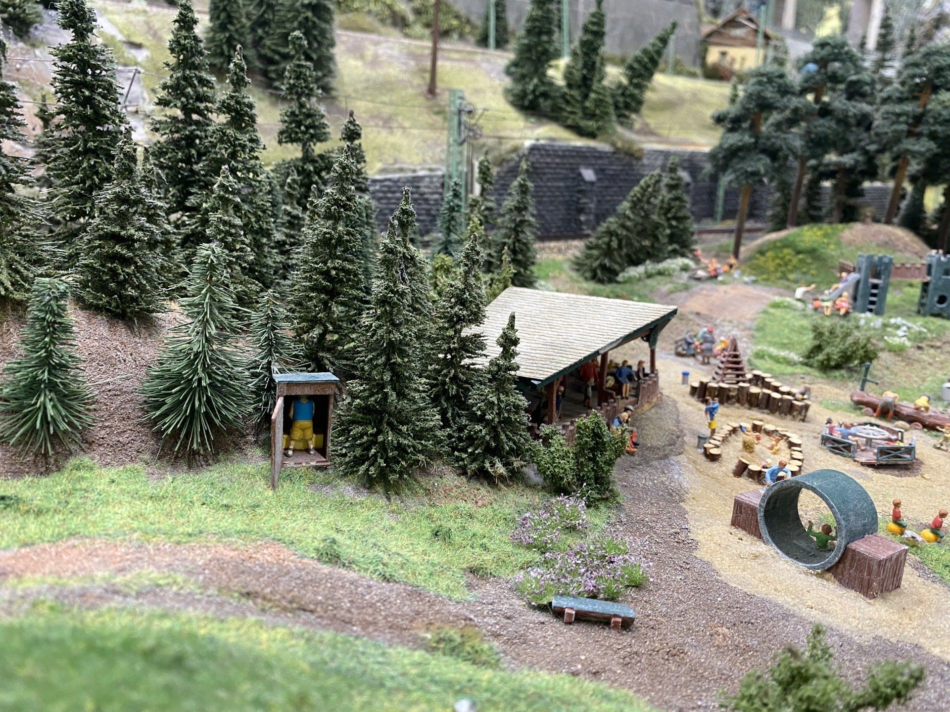 Miniaturdiorama: Waldgebiet mit kleinem Unterstand, Weg und Spielplatz; Grün- und Brauntöne.