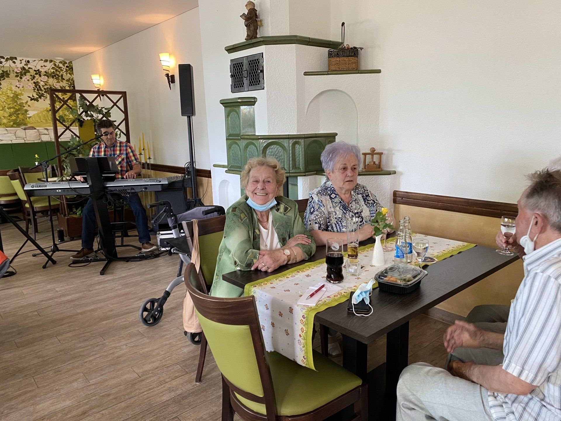 Zwei lächelnde Frauen an einem Tisch, neben einem Keyboard spielenden Musiker. Restaurant-Ambiente.