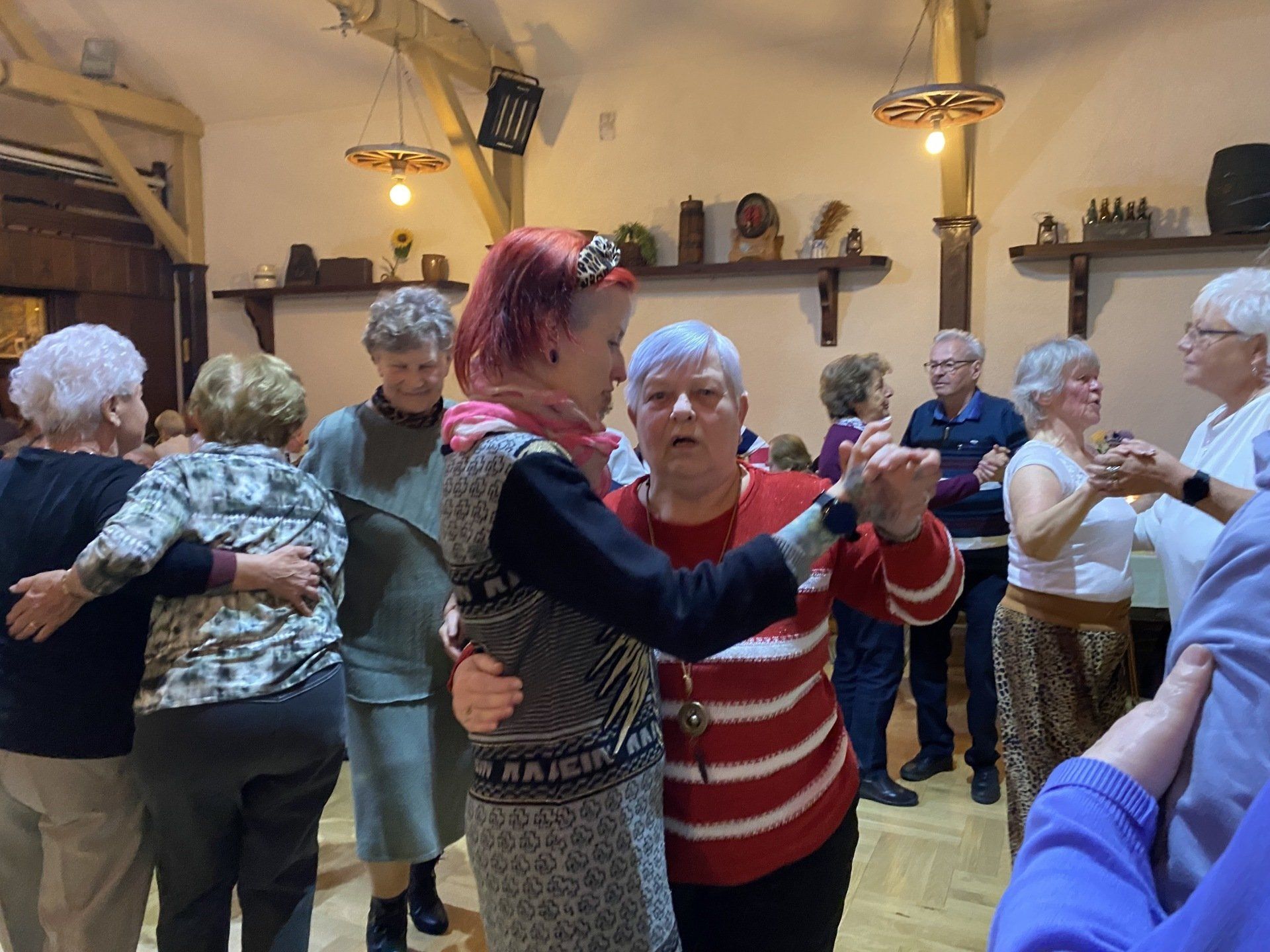 Menschen tanzen in einer Halle mit Holzbalken. 