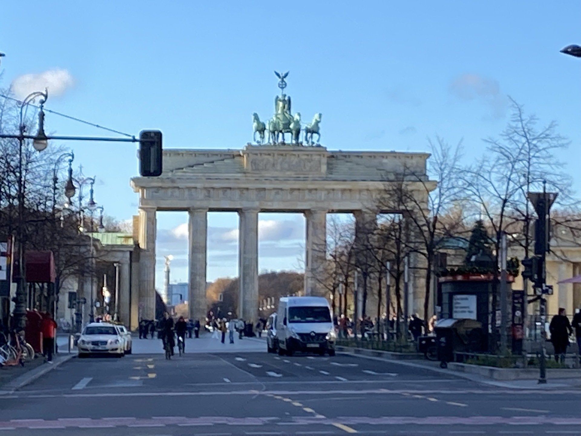 Brandenburger Tor in Berlin, Deutschland; ein großer Torbogen mit einer Streitwagenstatue, Autos, Fußgängern und Bäumen.