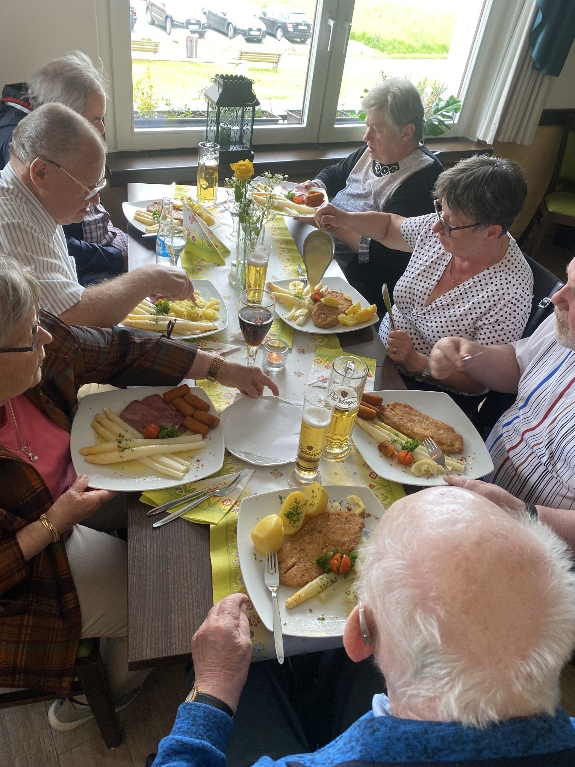 Menschen sitzen um einen Tisch herum und genießen in einem Restaurant eine Mahlzeit mit Fisch, Kartoffeln und Gemüse.