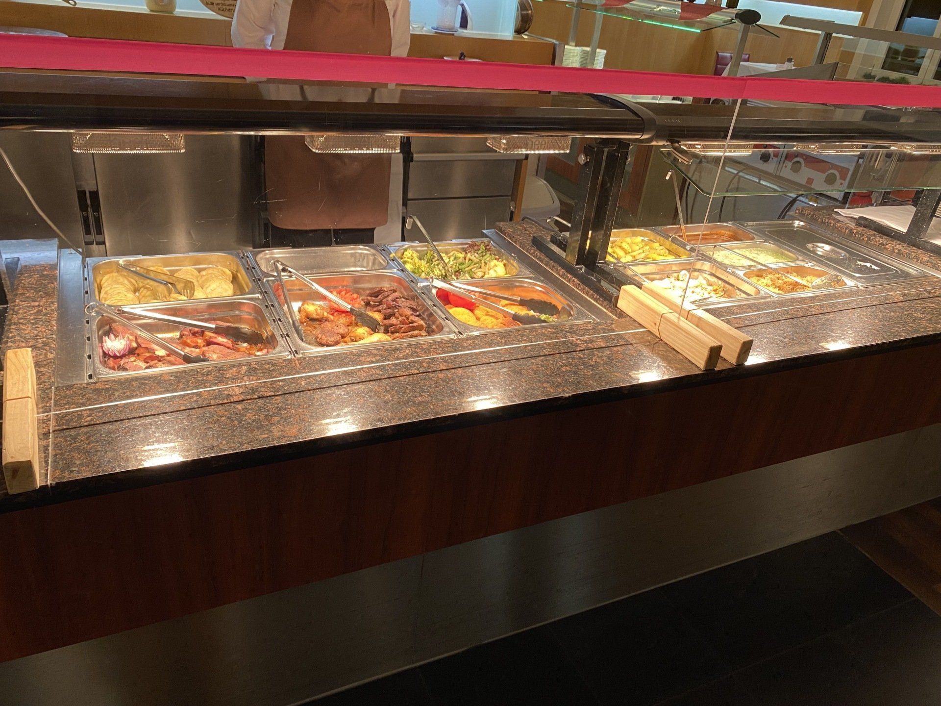 Buffet-Speisenpräsentation mit verschiedenen Gerichten in Metallbehältern, unter warmem Licht, aus Braun- und Edelstahl.